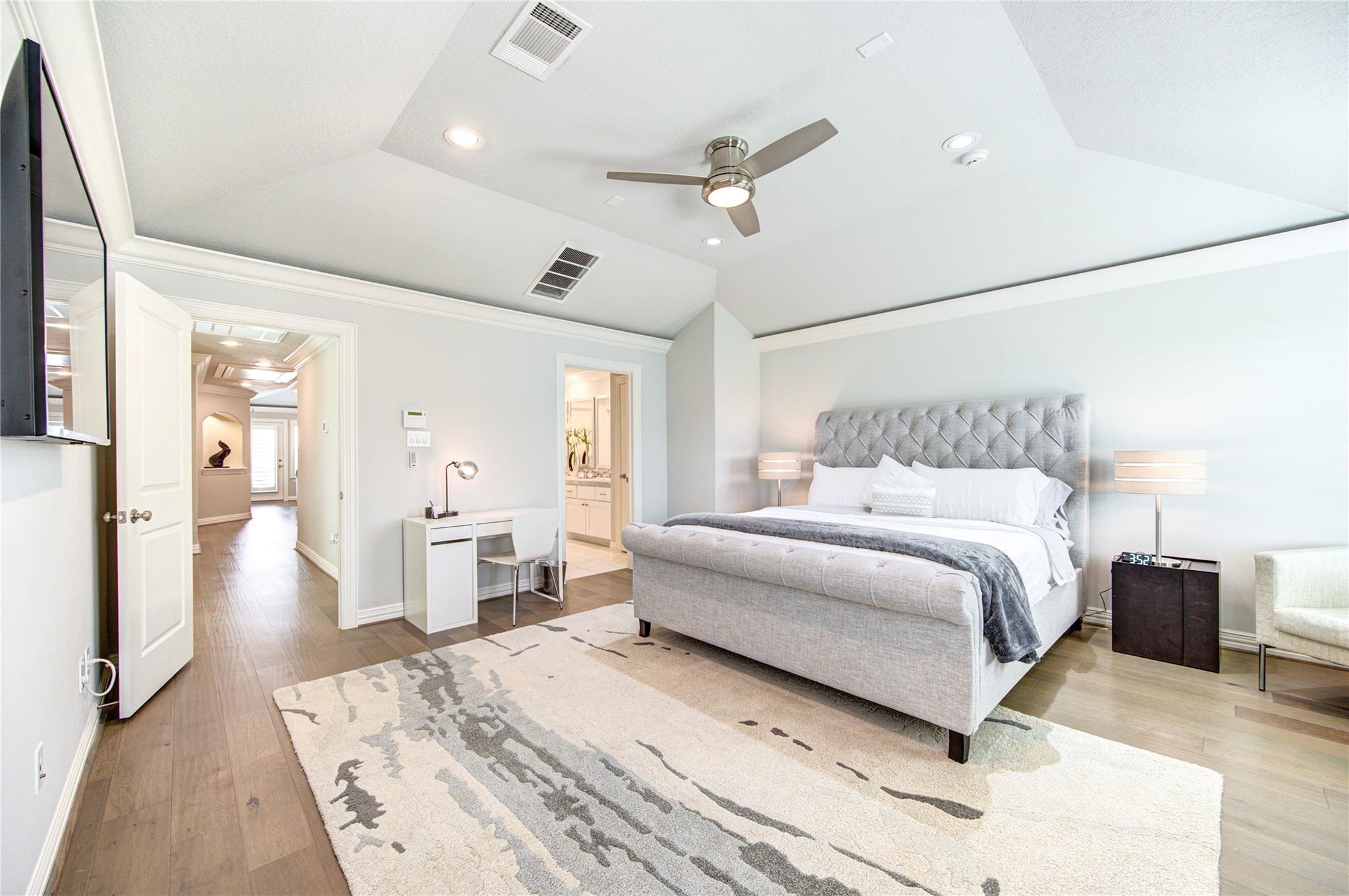 Furnished bedroom with a gray tufted bed, patterned rug, ceiling fan, and desk.