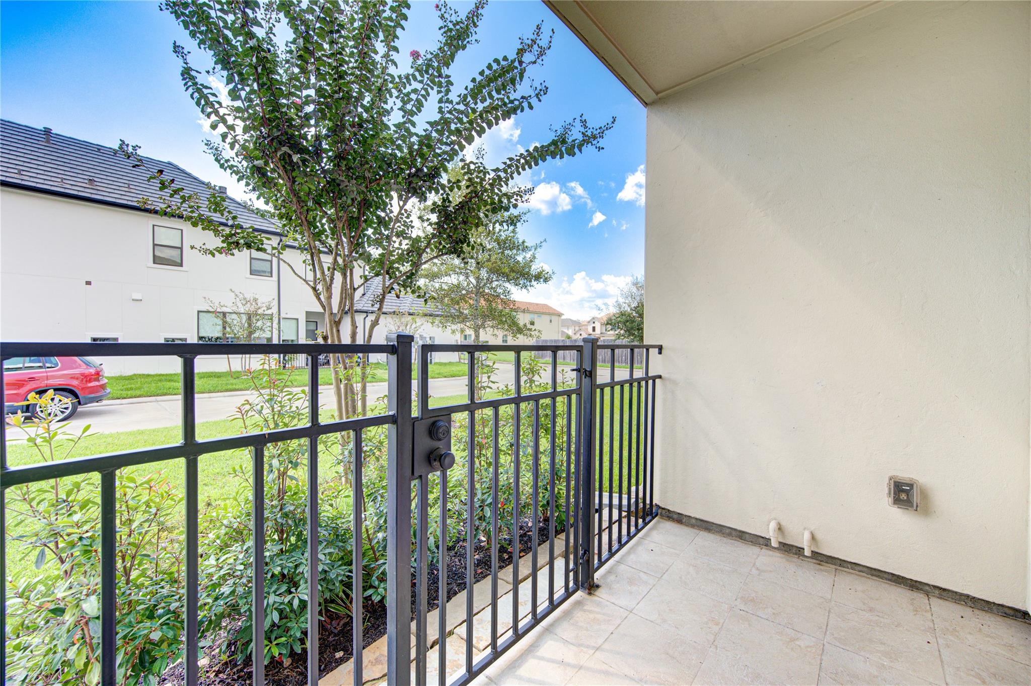 Covered tiled patio with a black metal railing and gate overlooking a landscaped garden.