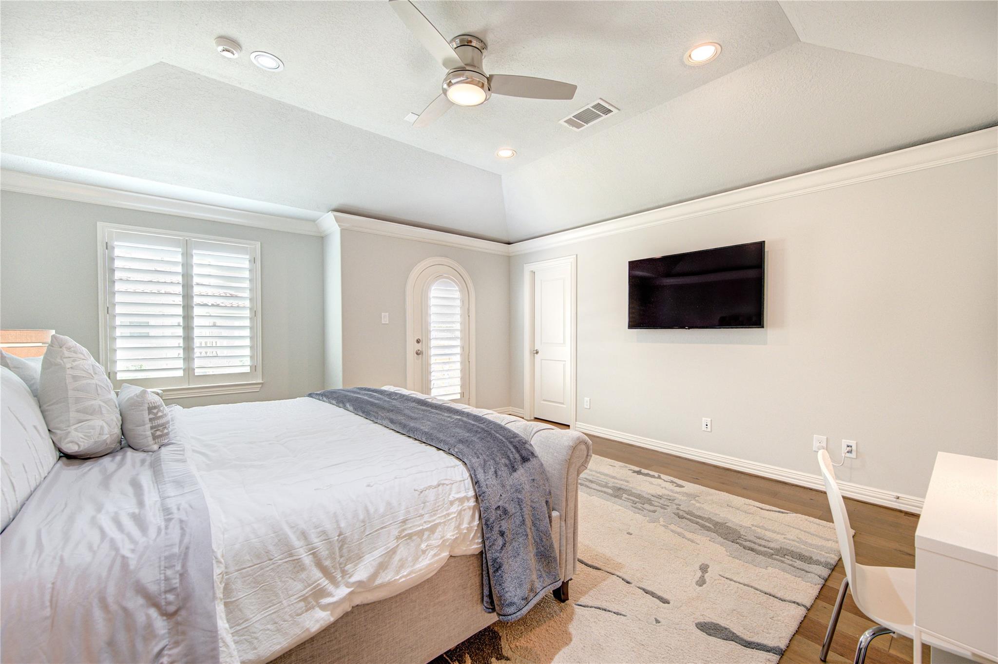 Bedroom with a large bed, plantation shutters, an arched door, and a wall-mounted television.