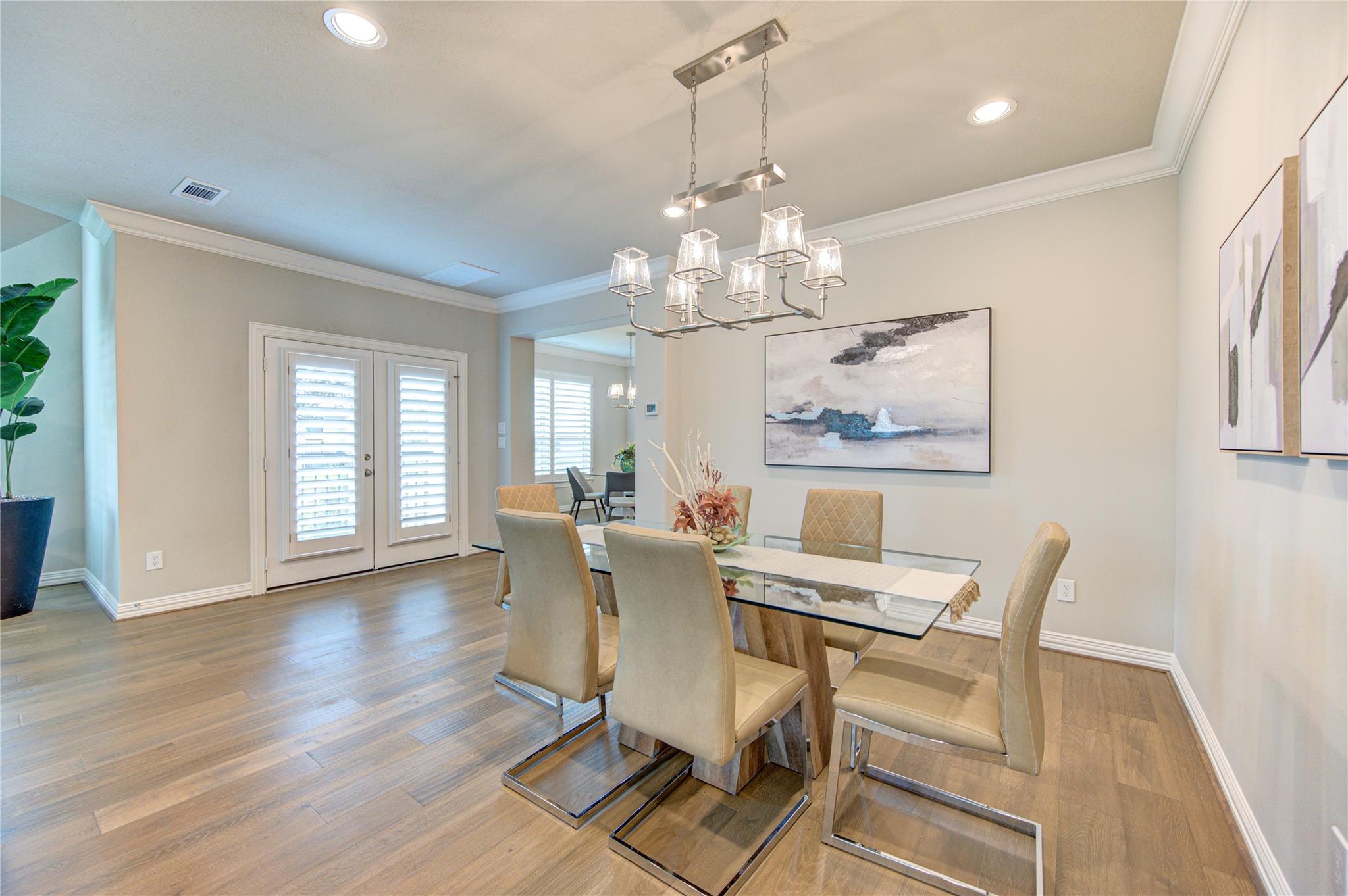 Dining room with a glass-top table, upholstered chairs, chandelier, and plantation shutters.