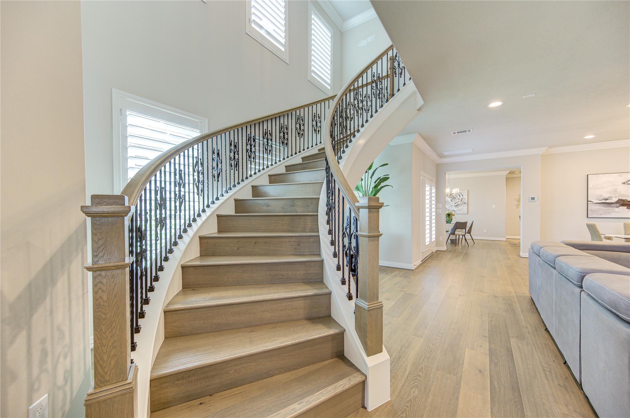 Foyer with a sweeping wood staircase, ornate iron railings, and tall shuttered windows.