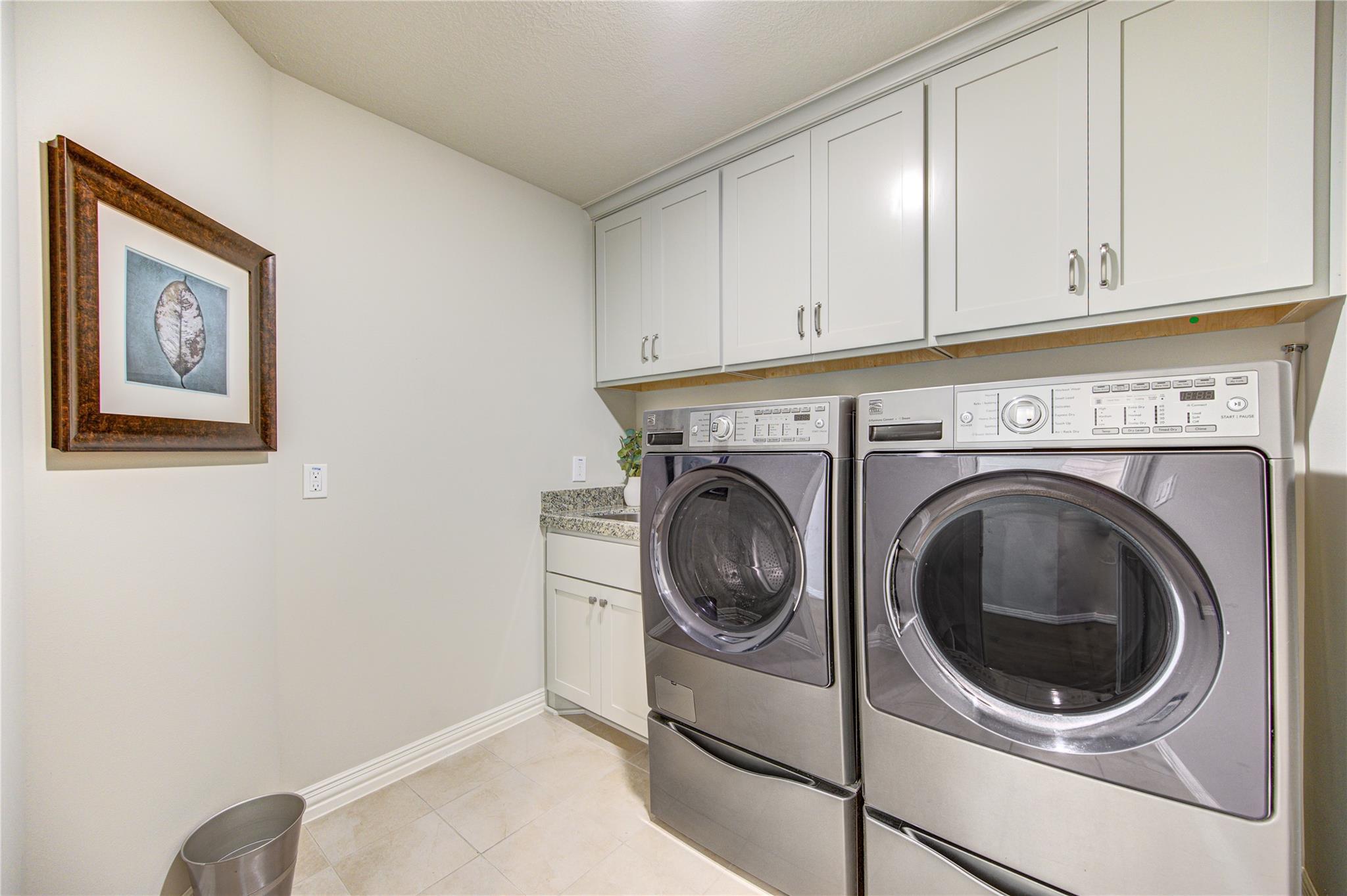Laundry room with stainless front-loading washer and dryer beneath white cabinets.