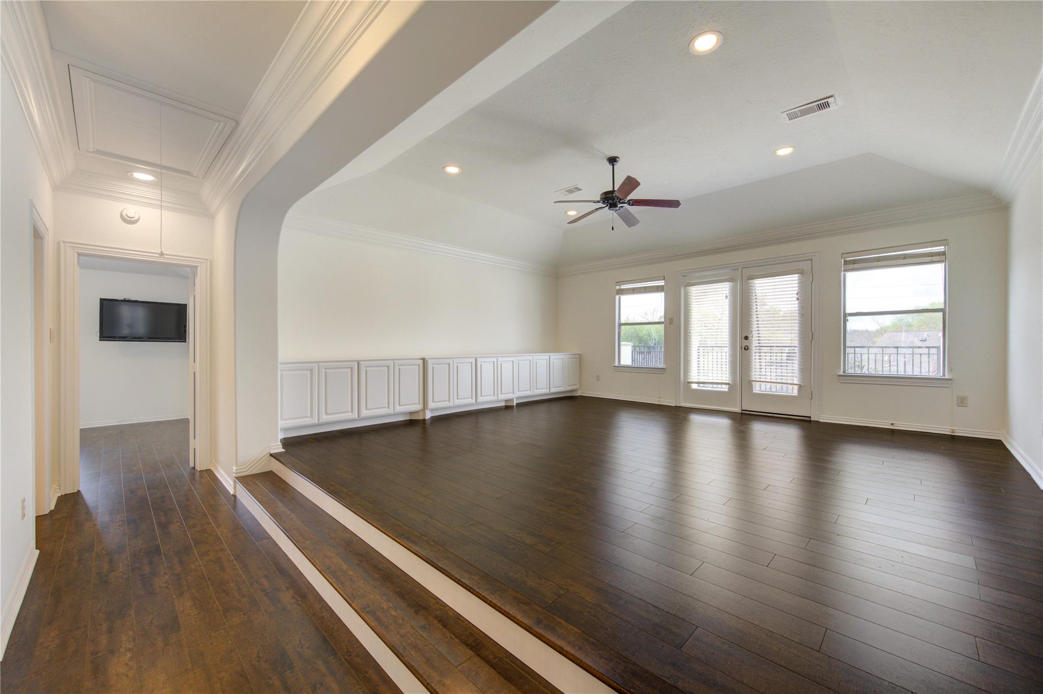 Empty room with dark hardwood floors, built-in cabinets, and French doors opening to a balcony.