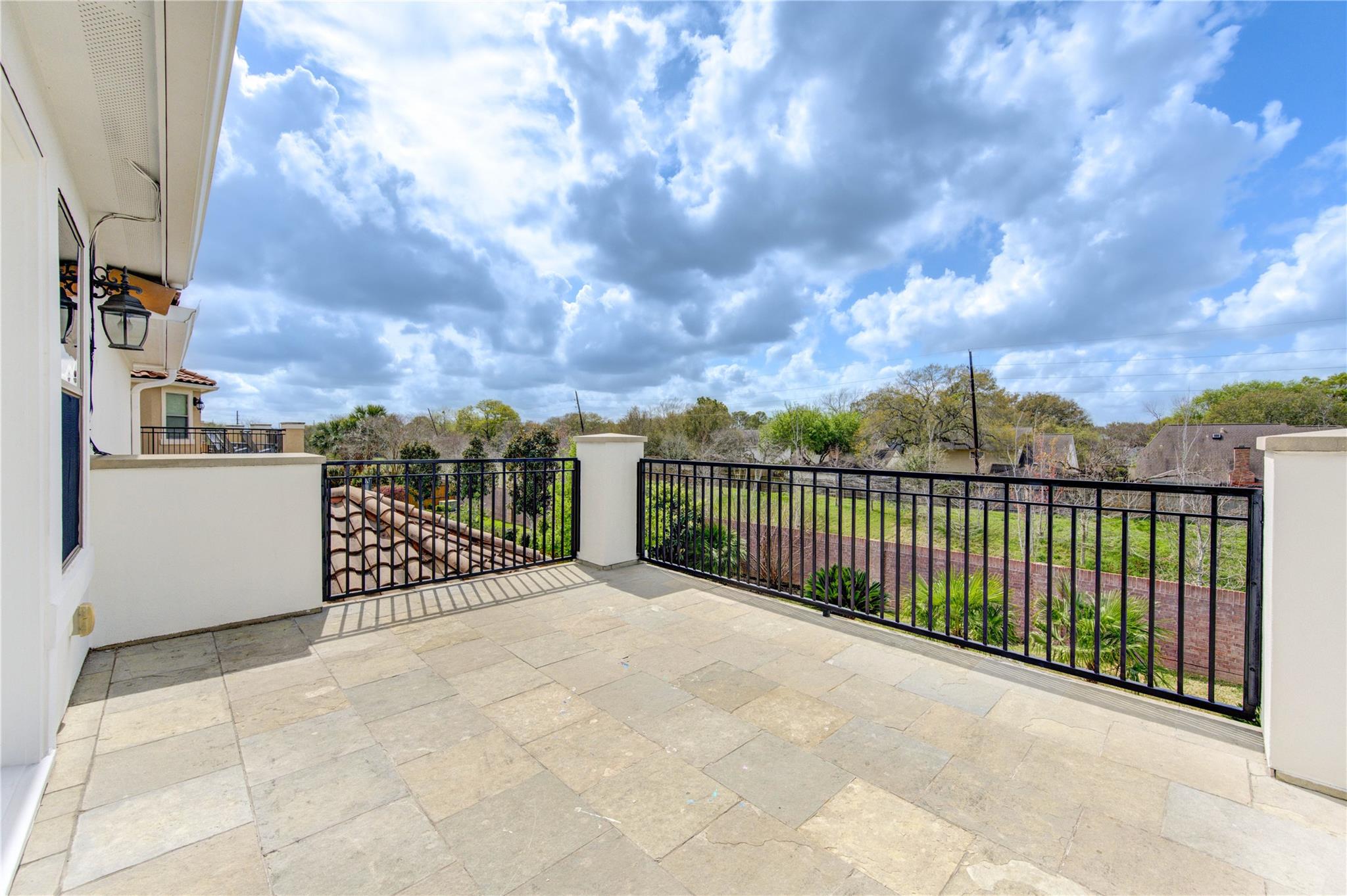 Stone-tiled terrace with black railings overlooking a green yard and neighboring homes.