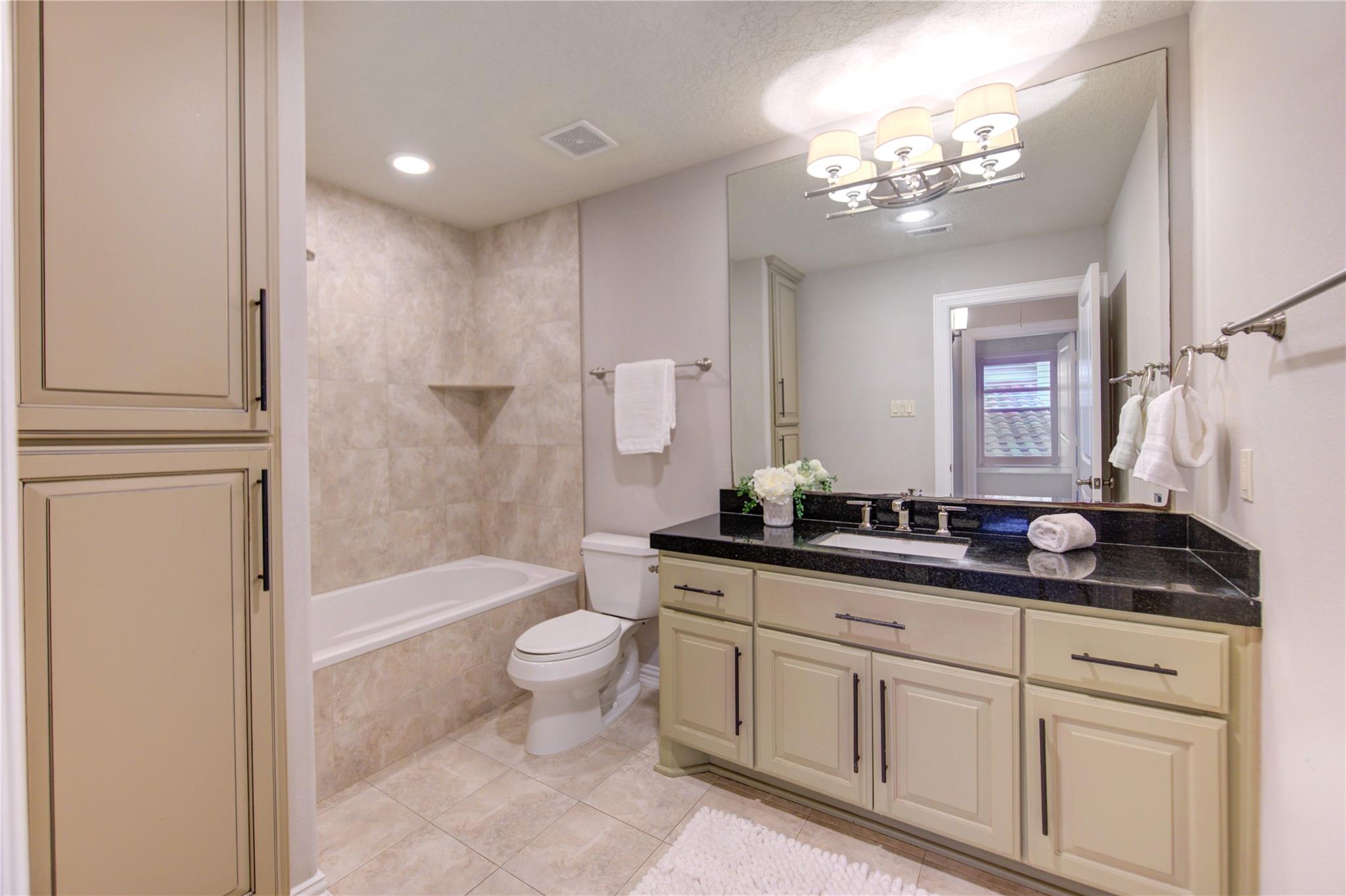 Bathroom with a tiled bathtub, cream built-in vanity, black granite countertop, and large mirror.