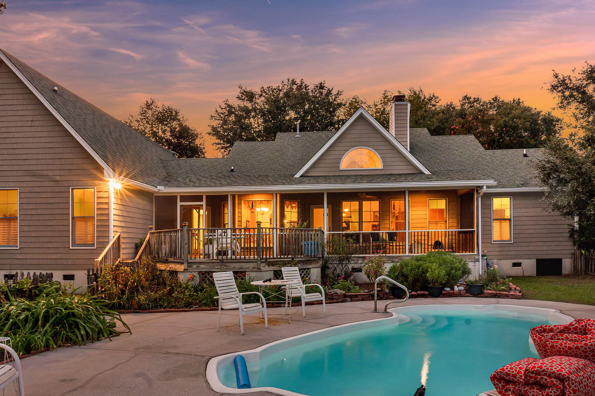 Gray-sided home with a covered deck and swimming pool at dusk.