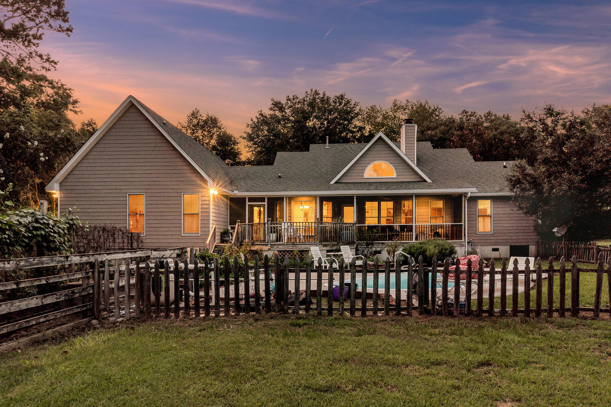 House at dusk with a covered rear porch and fenced backyard pool.