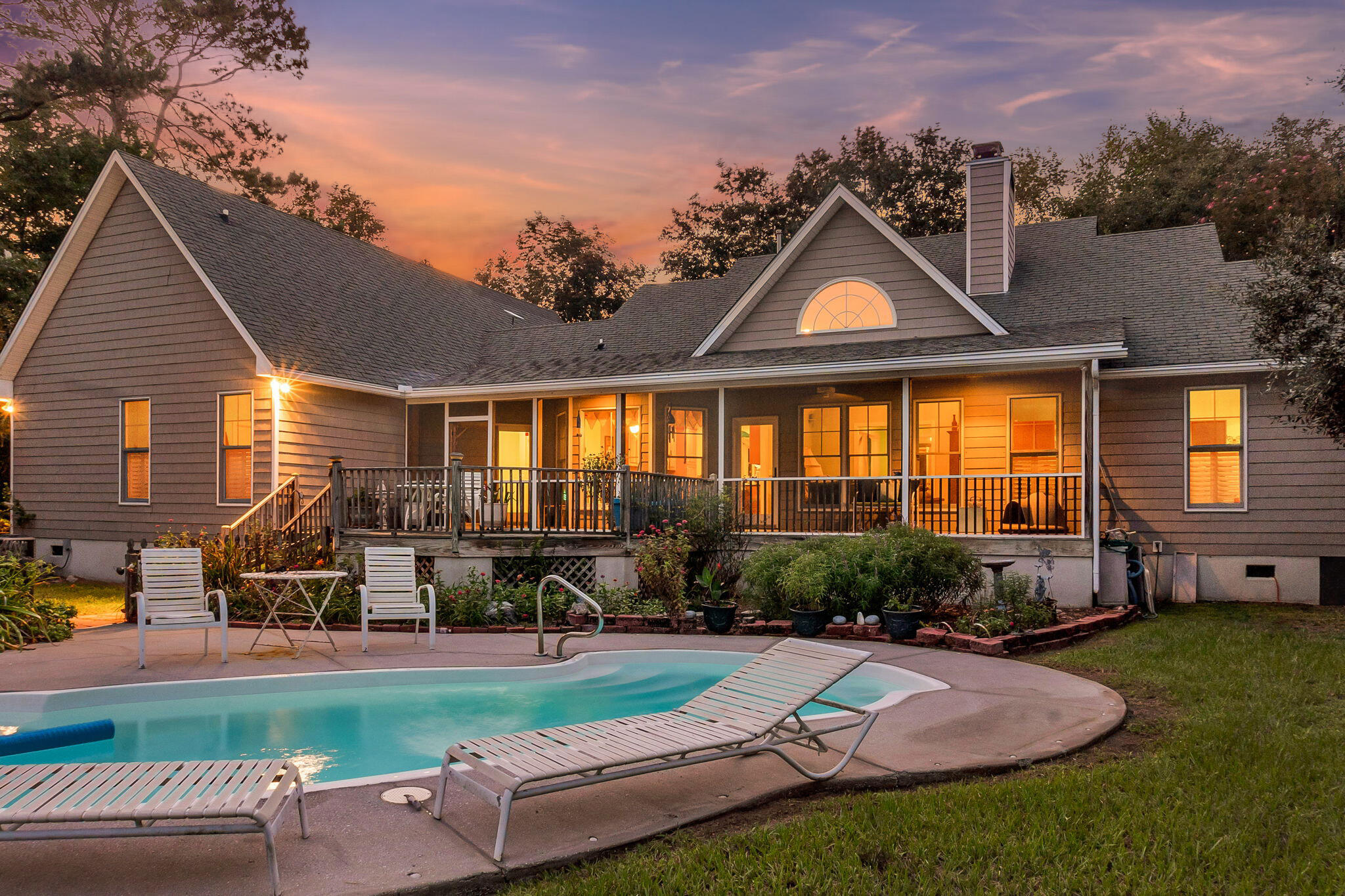 Gray gabled house with a covered porch and swimming pool at dusk.