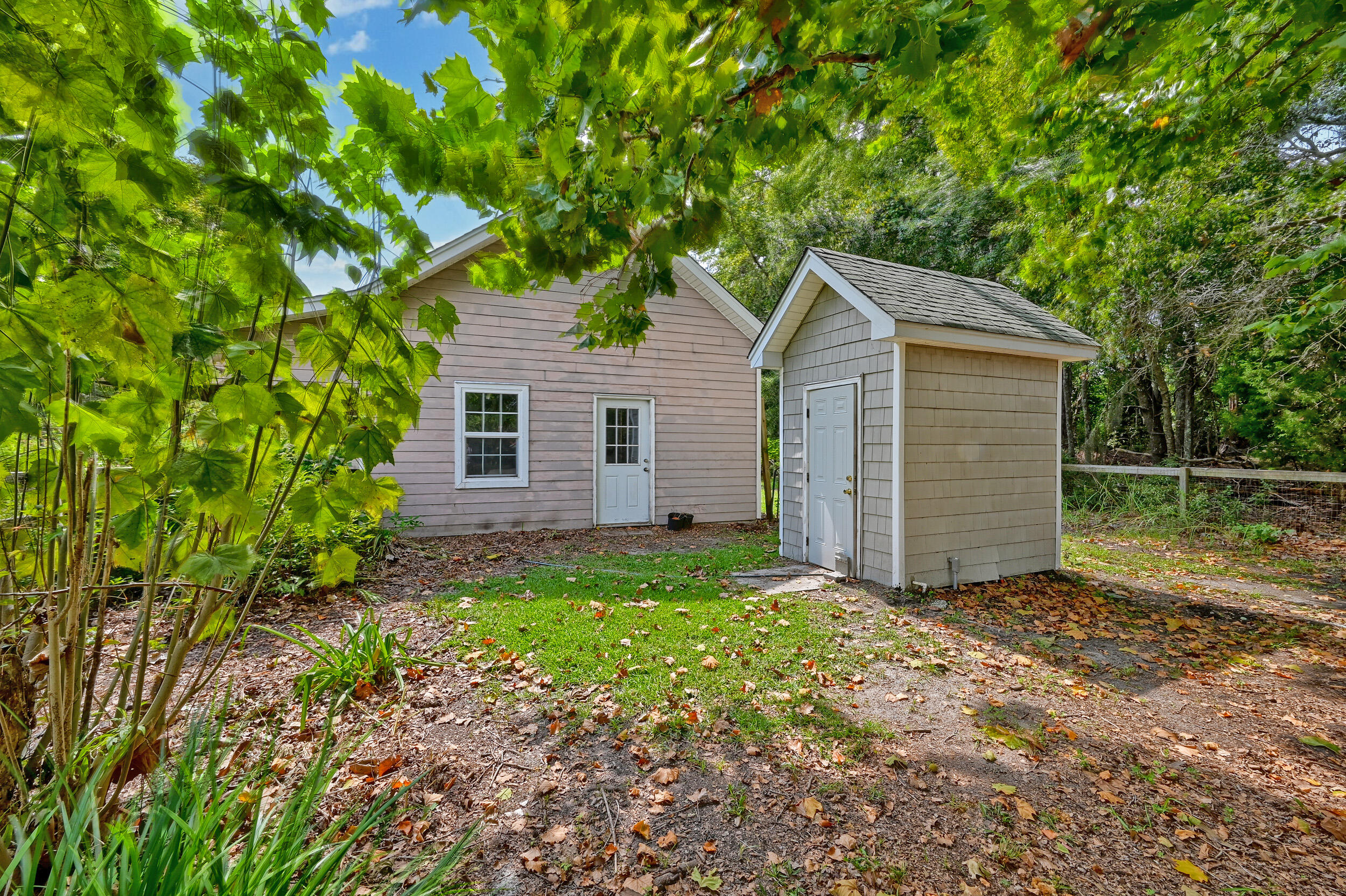 Light-colored house and detached outbuilding in a leafy, wooded yard.