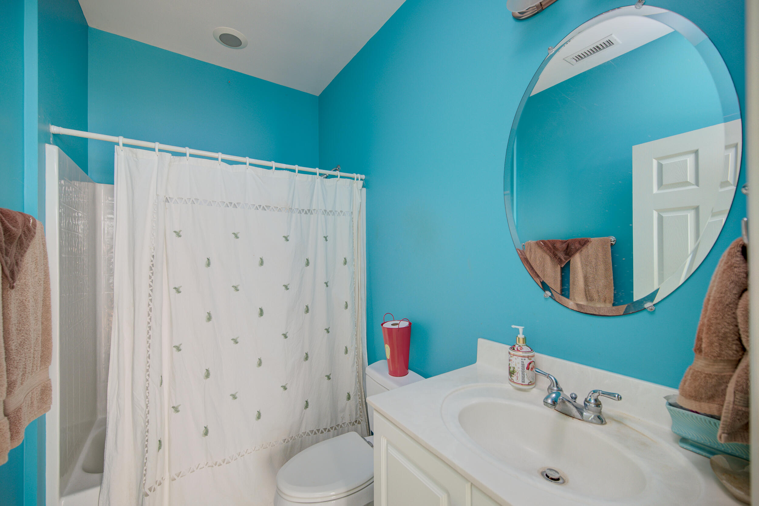 Bathroom with turquoise walls, a white shower curtain, and a large round mirror above the vanity.