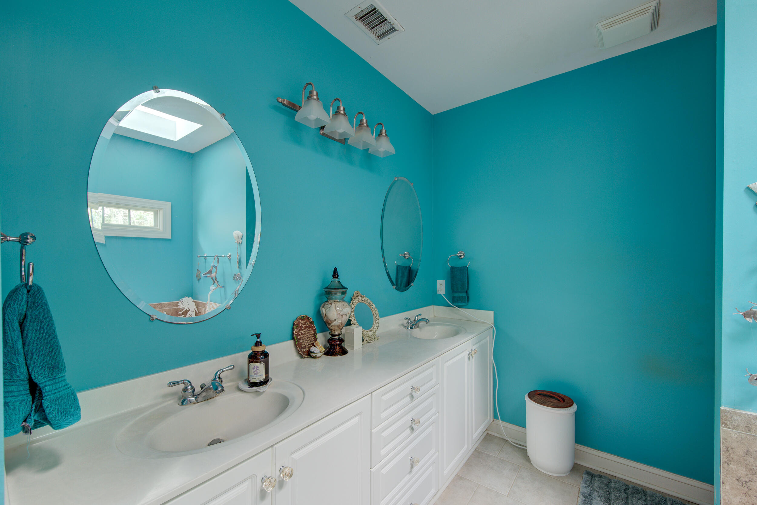 Bathroom with turquoise walls, a long white double vanity, and large oval mirrors.