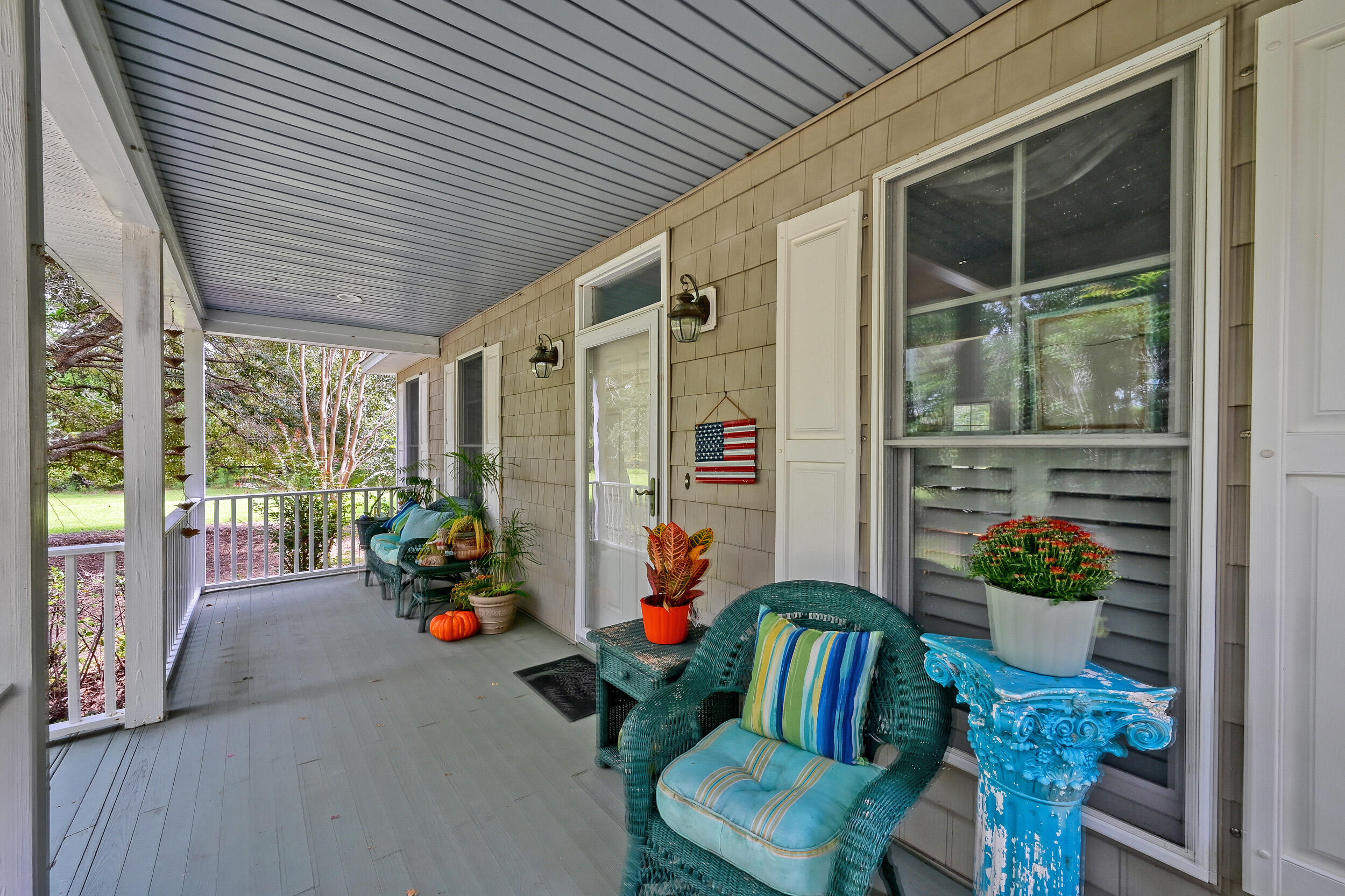 Covered front porch with blue-cushioned wicker chairs, potted plants, and a view of the leafy yard.