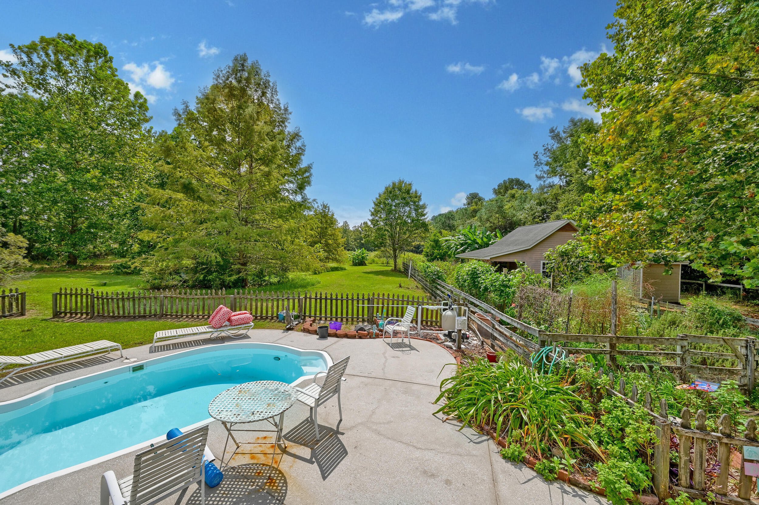 Backyard swimming pool and patio with lounge chairs, fenced lawn, and mature trees.