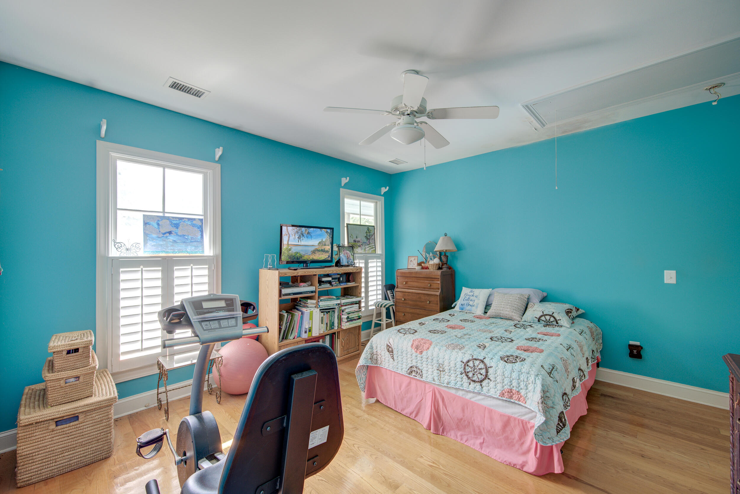 Turquoise bedroom with a nautical quilt, plantation shutters, and exercise equipment.