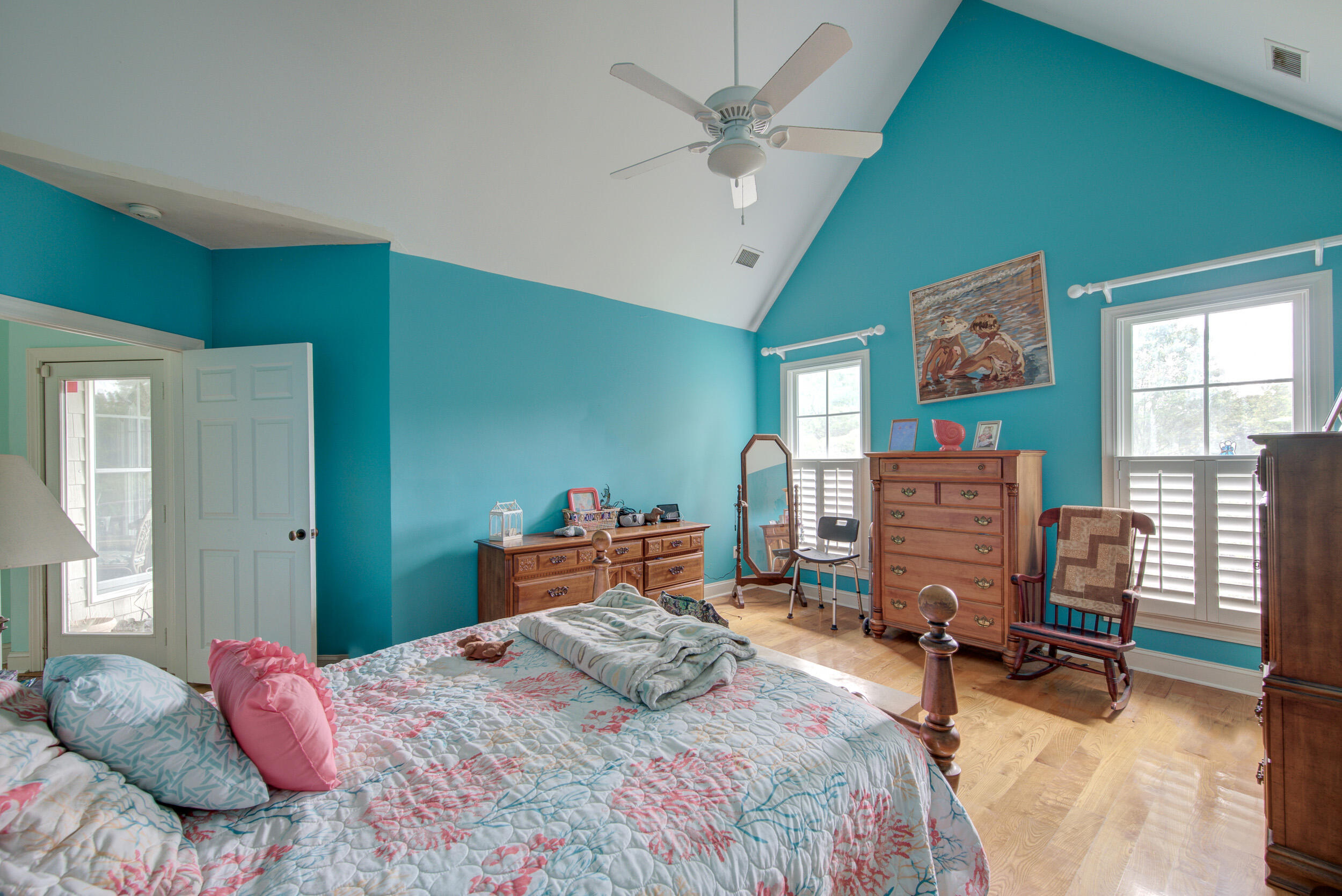 Furnished bedroom with teal walls, vaulted ceiling, floral bedding, and hardwood floors.