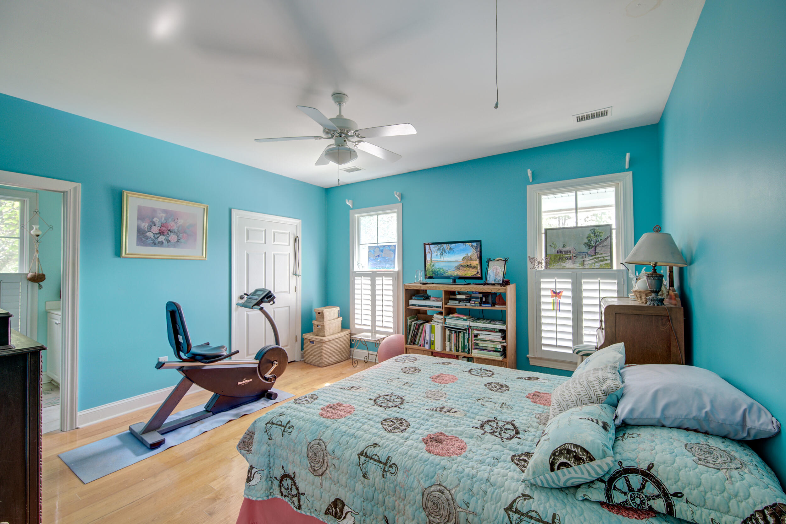 Turquoise bedroom with a patterned bed, exercise bike, and shuttered windows.