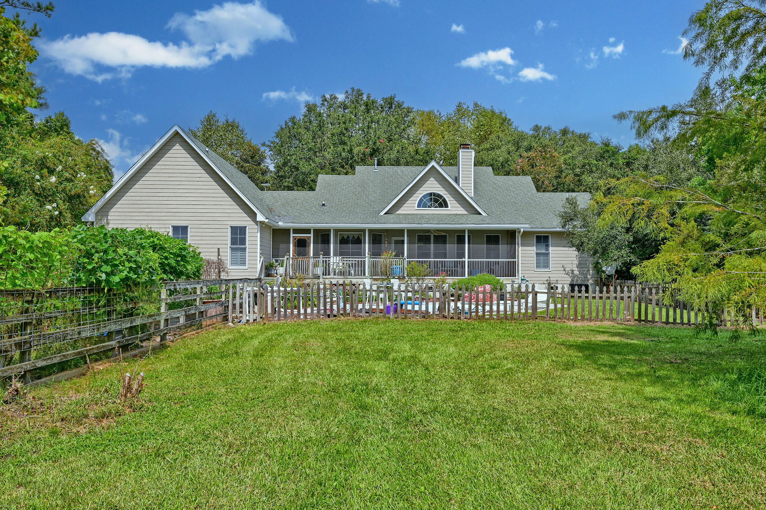 Home’s rear exterior with a screened porch, fenced pool, and spacious green lawn.