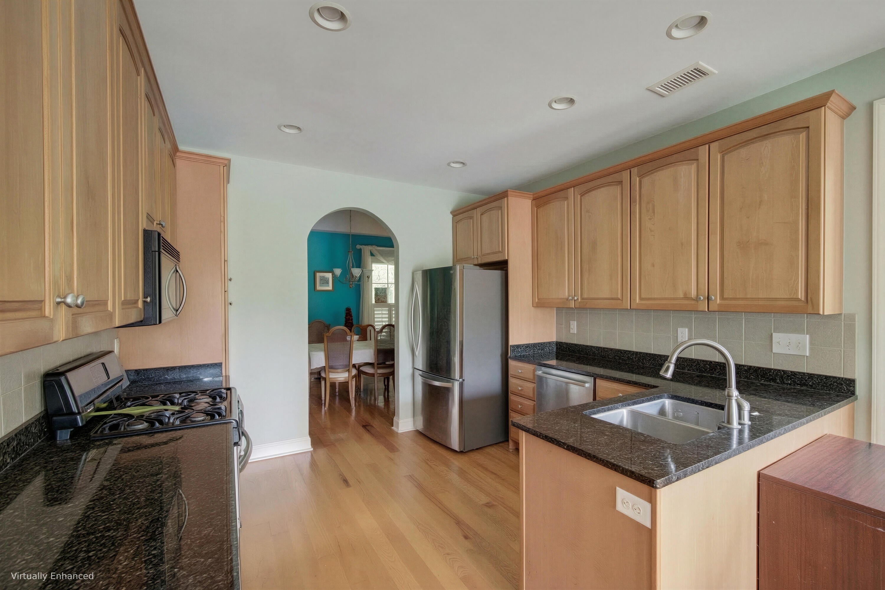 Kitchen with wood cabinets, dark granite counters, stainless steel appliances, and an arched opening to the dining area.