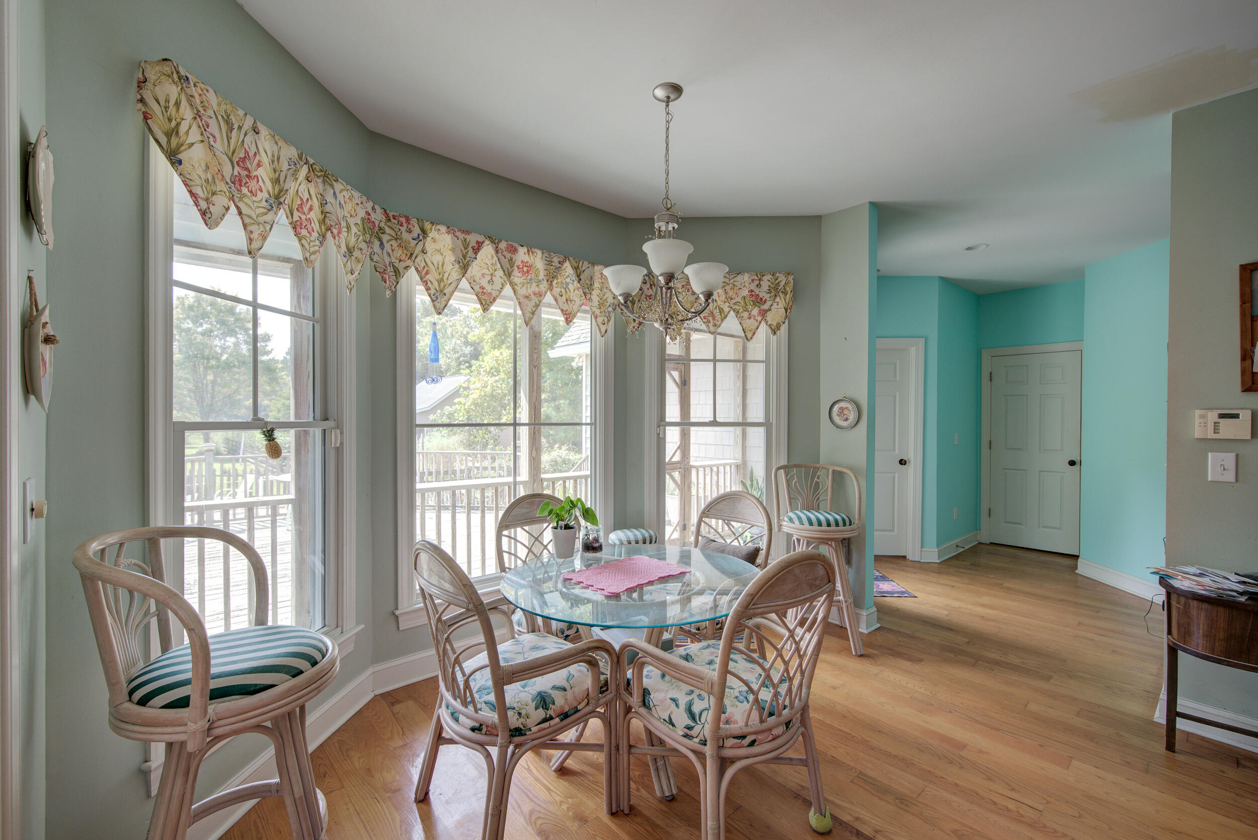 Dining area with a glass-top table, wicker chairs, tall windows, and floral valances.