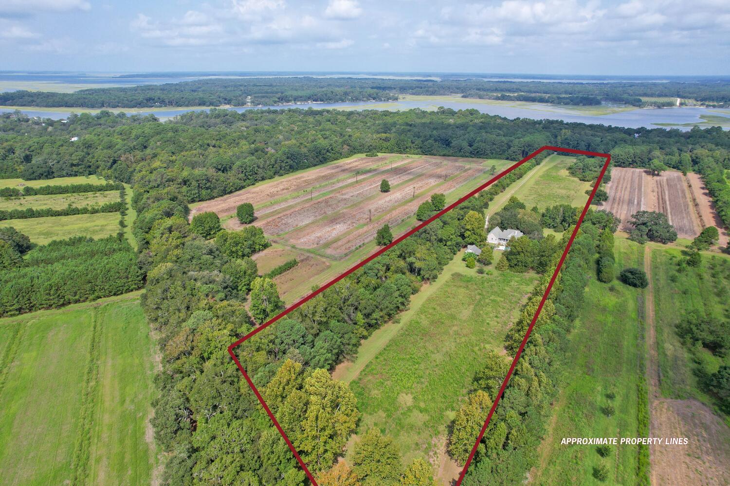 Aerial view of wooded acreage outlined in red, with a house, fields, and distant waterways.
