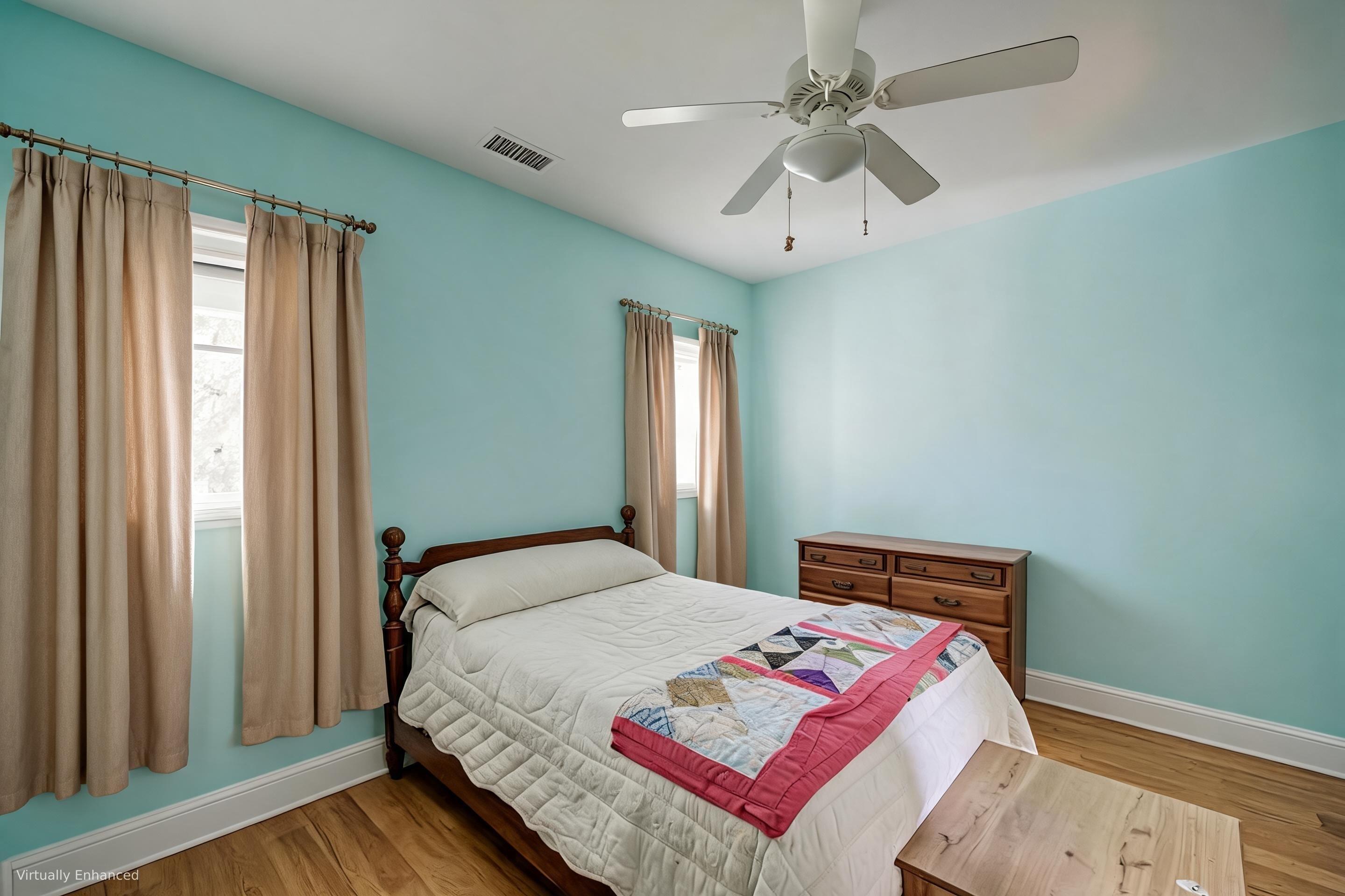 Bedroom with turquoise walls, a dark wood bed, colorful patchwork blanket, hardwood floors, and ceiling fan.