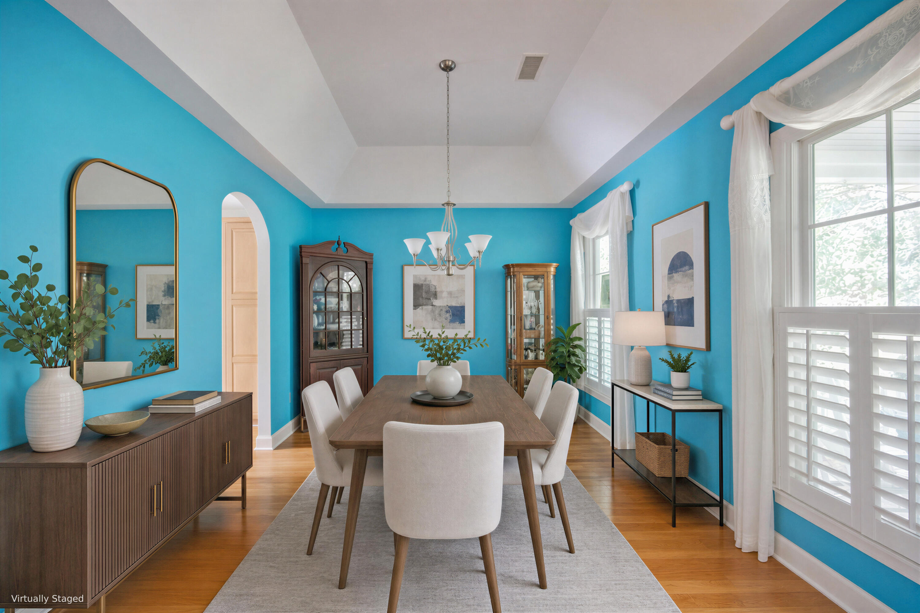 Dining room with turquoise walls, a wood table, white chairs, and large shuttered windows.