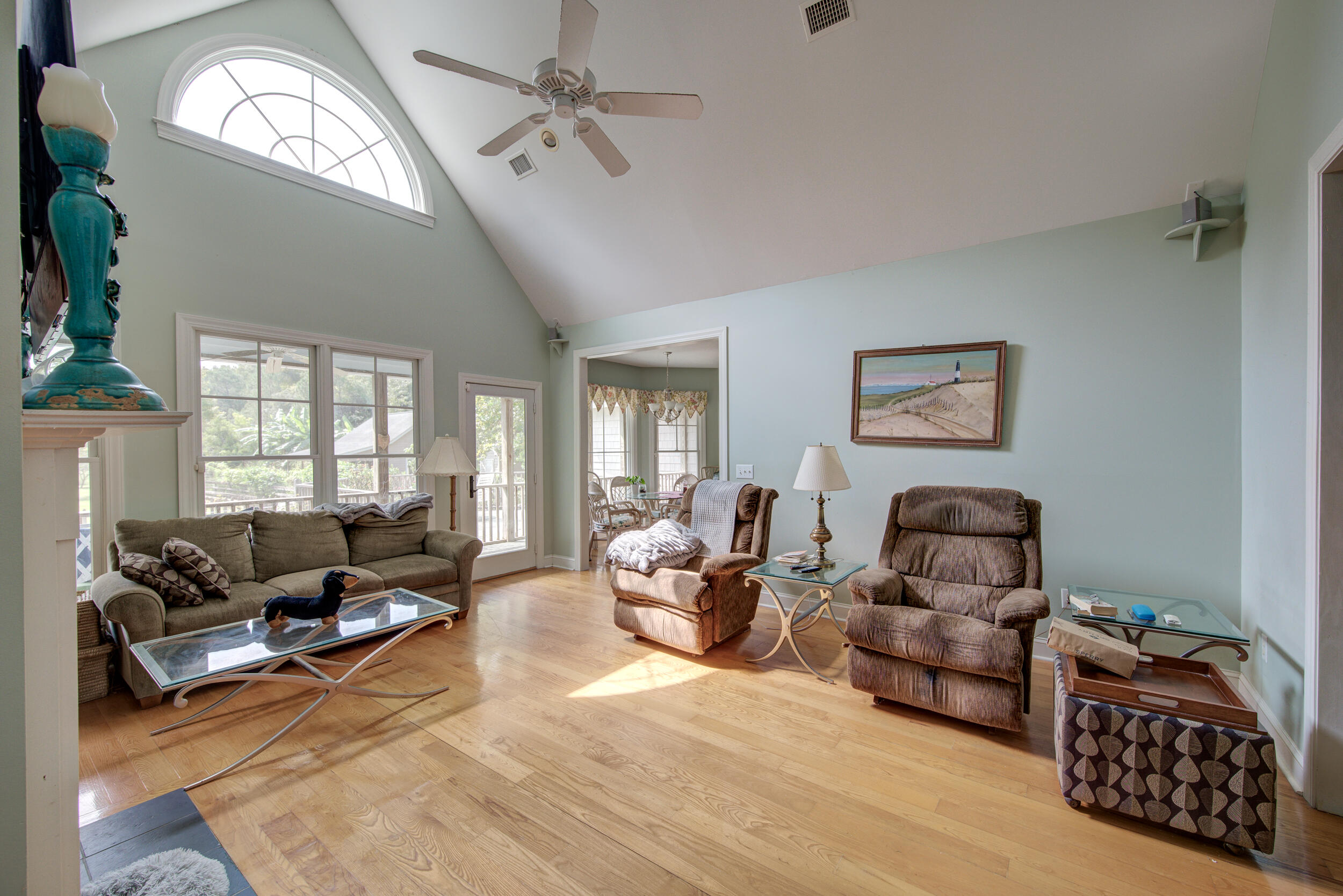 Living room with vaulted ceiling, arched window, hardwood floors, sofa, and recliners.