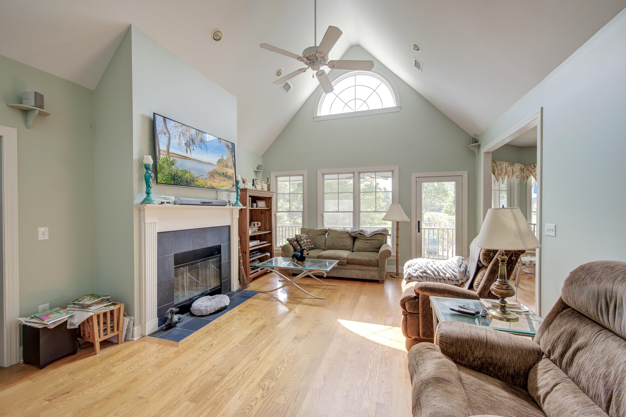 Vaulted living room with a fireplace, hardwood floors, large windows, and a glass door.