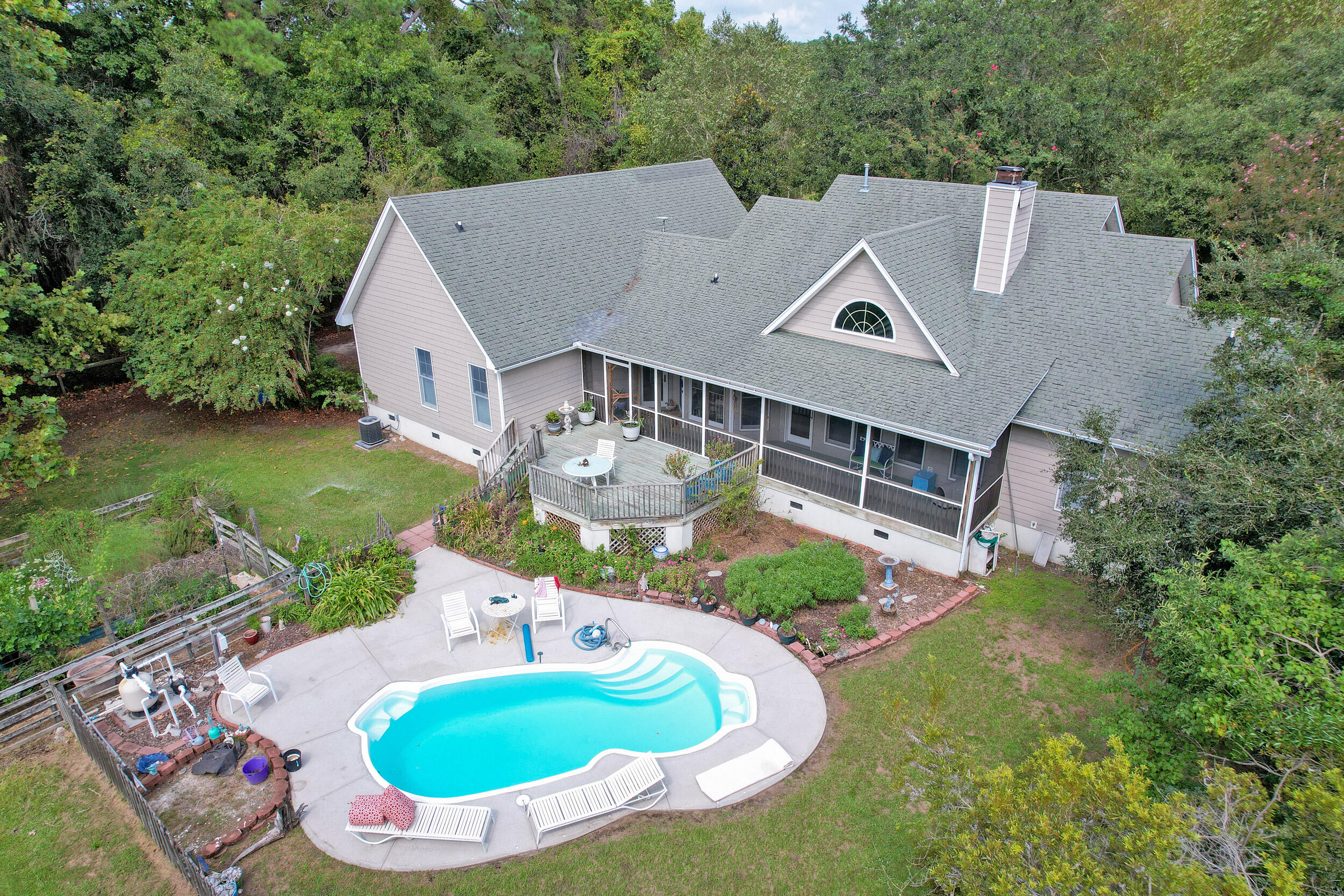 Aerial view of a house with a screened porch, raised deck, and curved pool in a wooded yard.