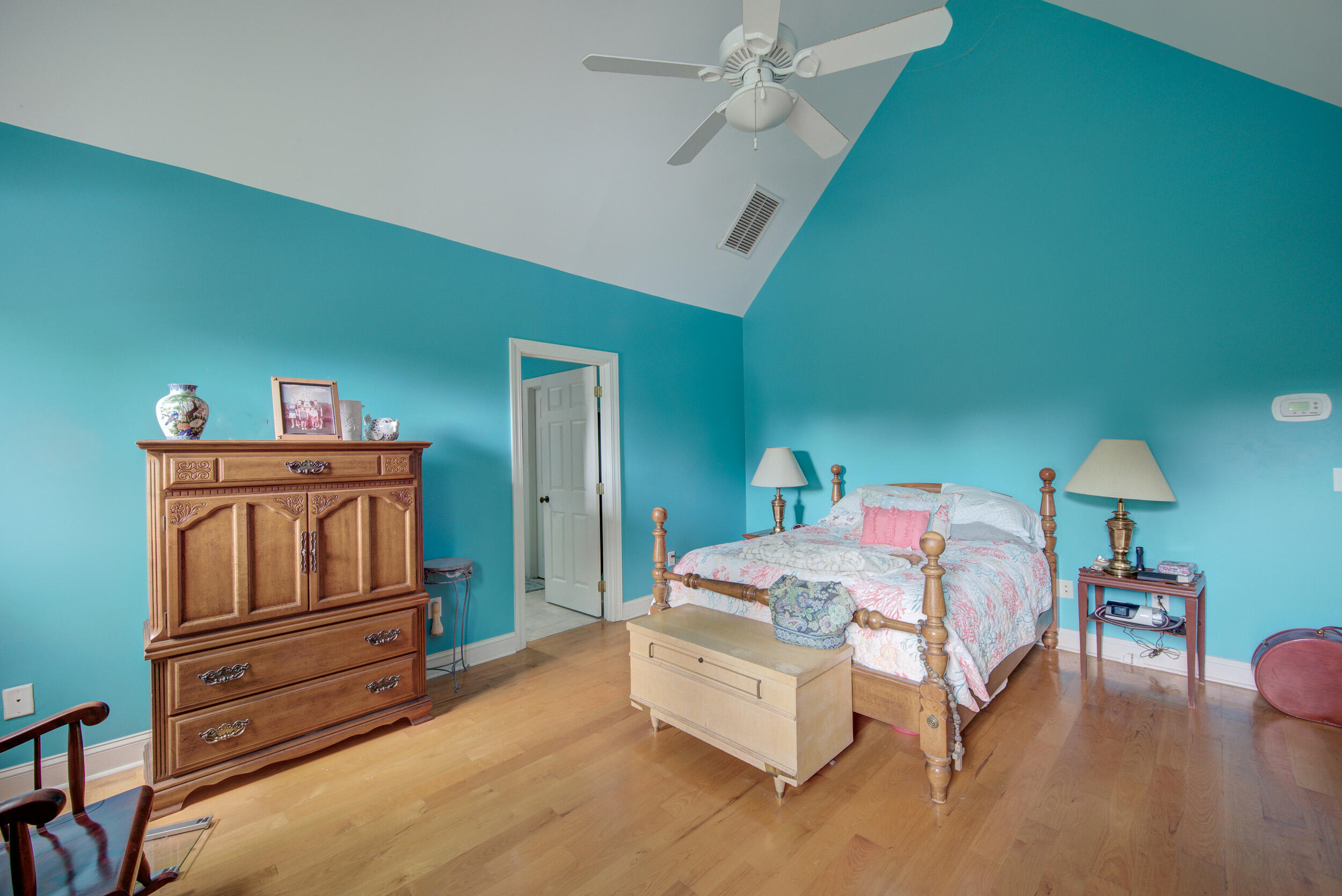 Bedroom with turquoise walls, a wooden four-poster bed, hardwood floors, and an ornate armoire.