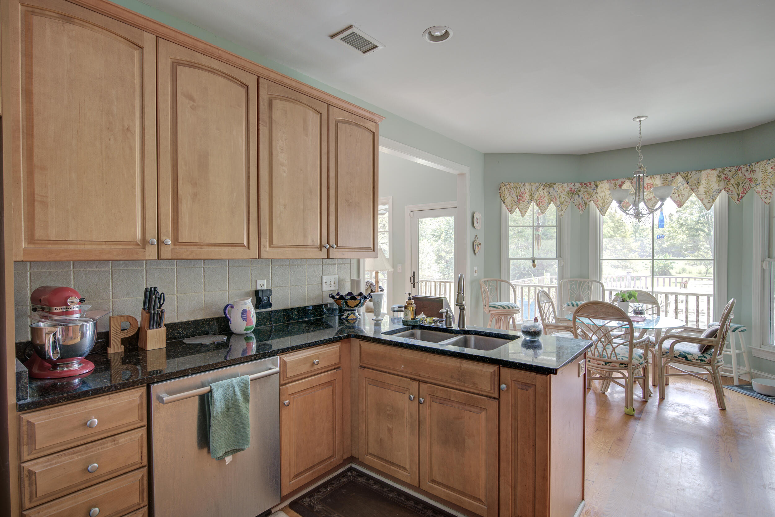 Kitchen with wood cabinets and granite counters opening to a bright dining area with large windows.