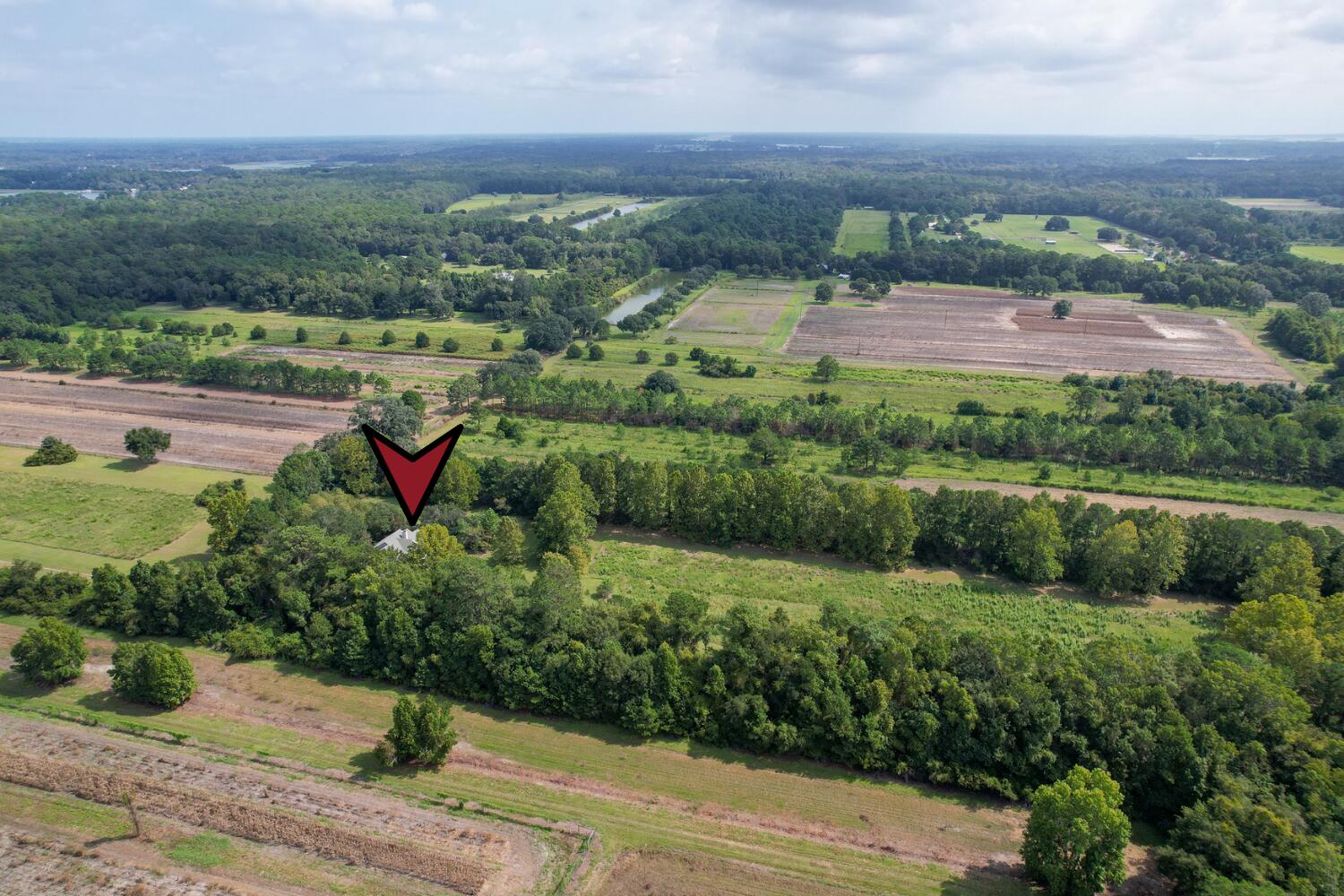 Aerial view of a small house marked by a red arrow, surrounded by wooded acreage and fields.