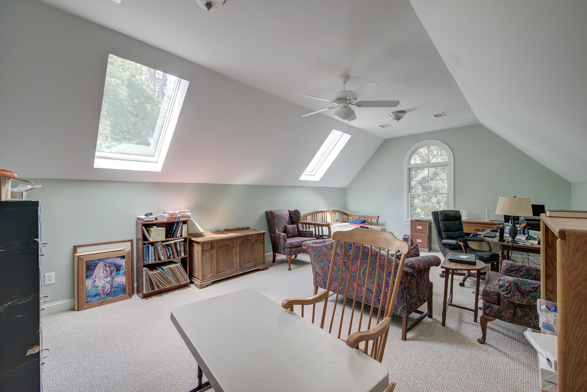 Furnished attic office and sitting area with a vaulted ceiling, skylights, and an arched window.