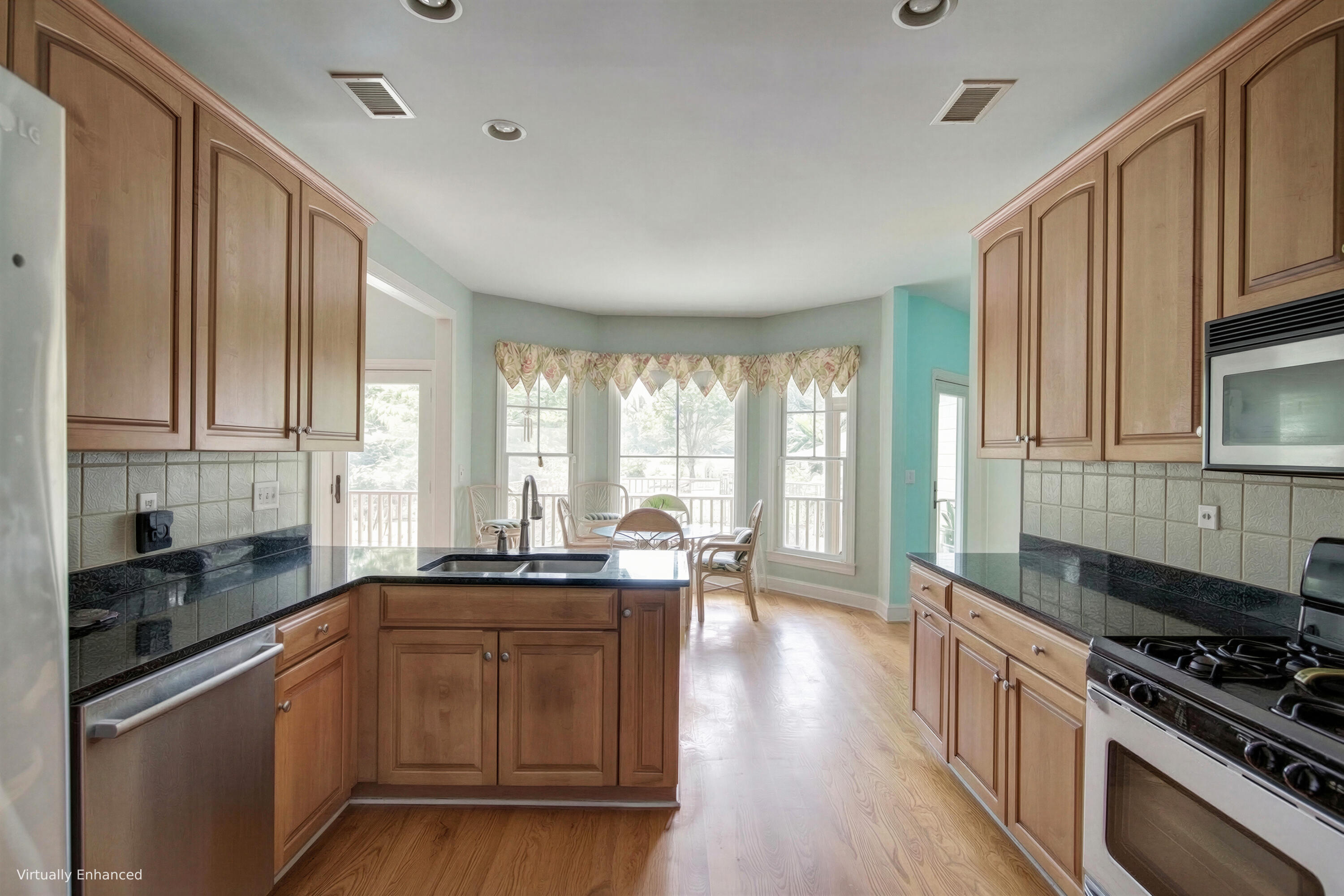 Kitchen with wood cabinetry and a central sink island, opening to a bright windowed dining nook.
