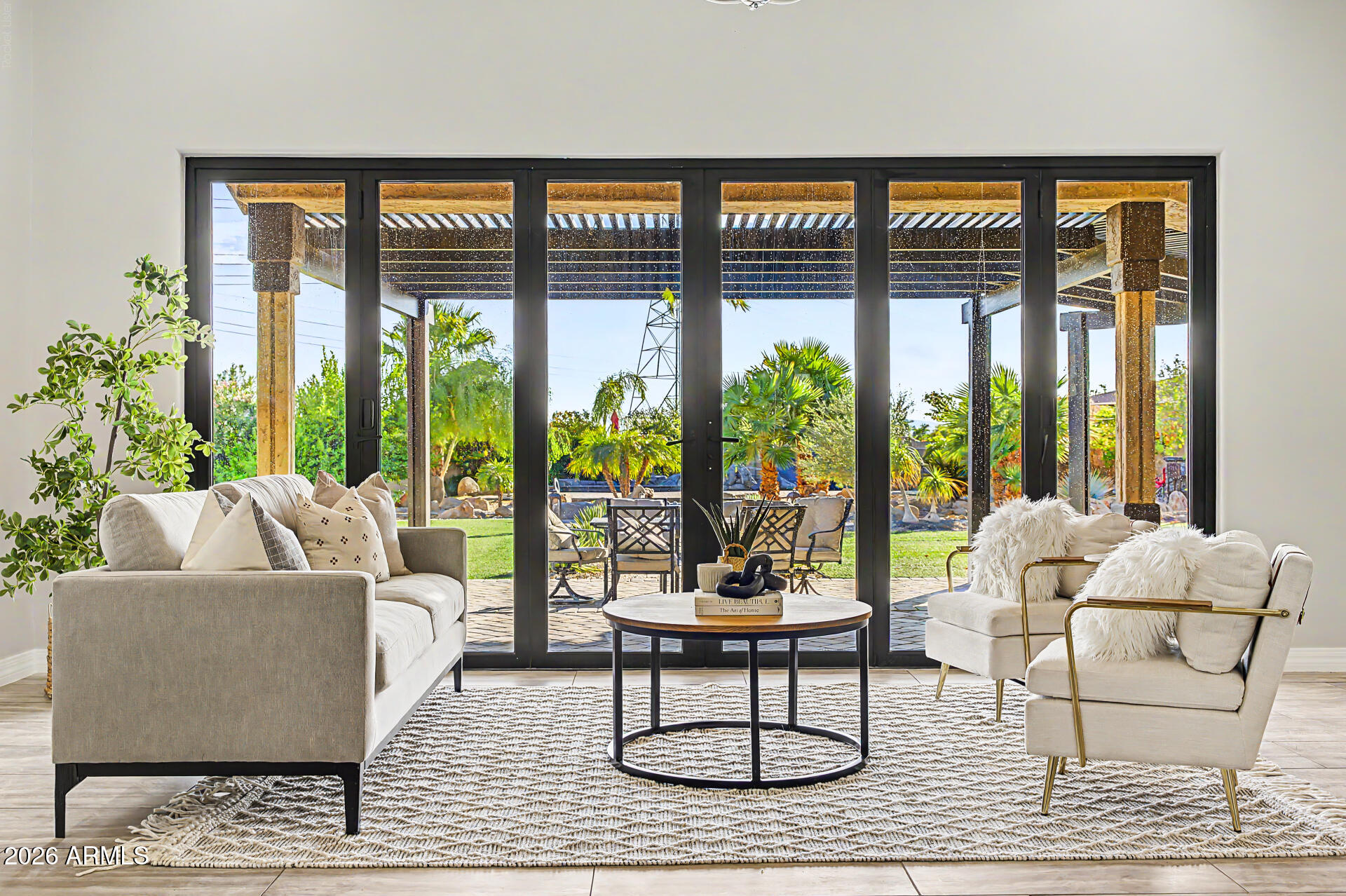 Living room with neutral seating and wide glass doors opening onto a palm-filled patio.