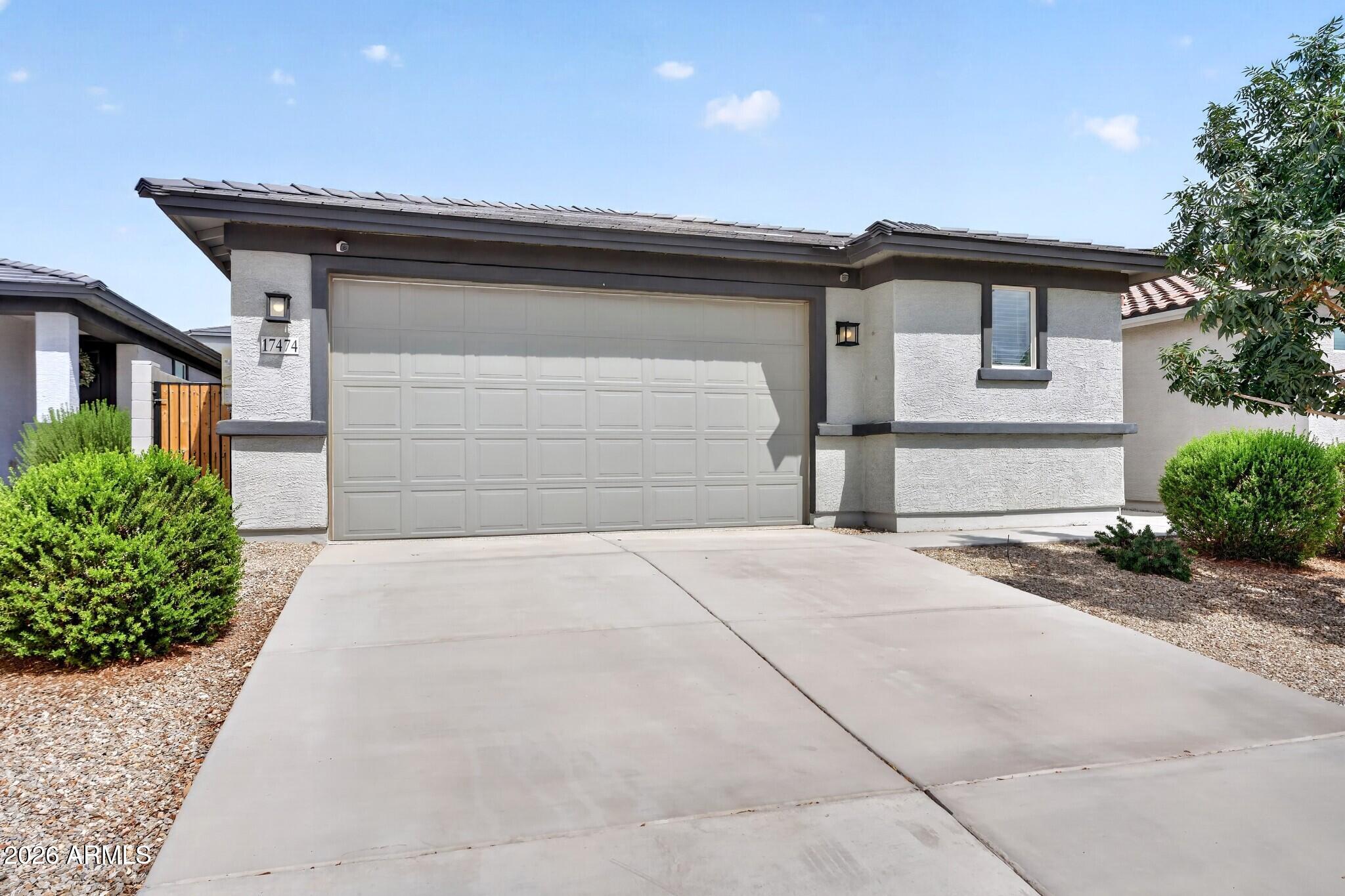 Single-story stucco home with a wide garage, long driveway, and gravel landscaping.