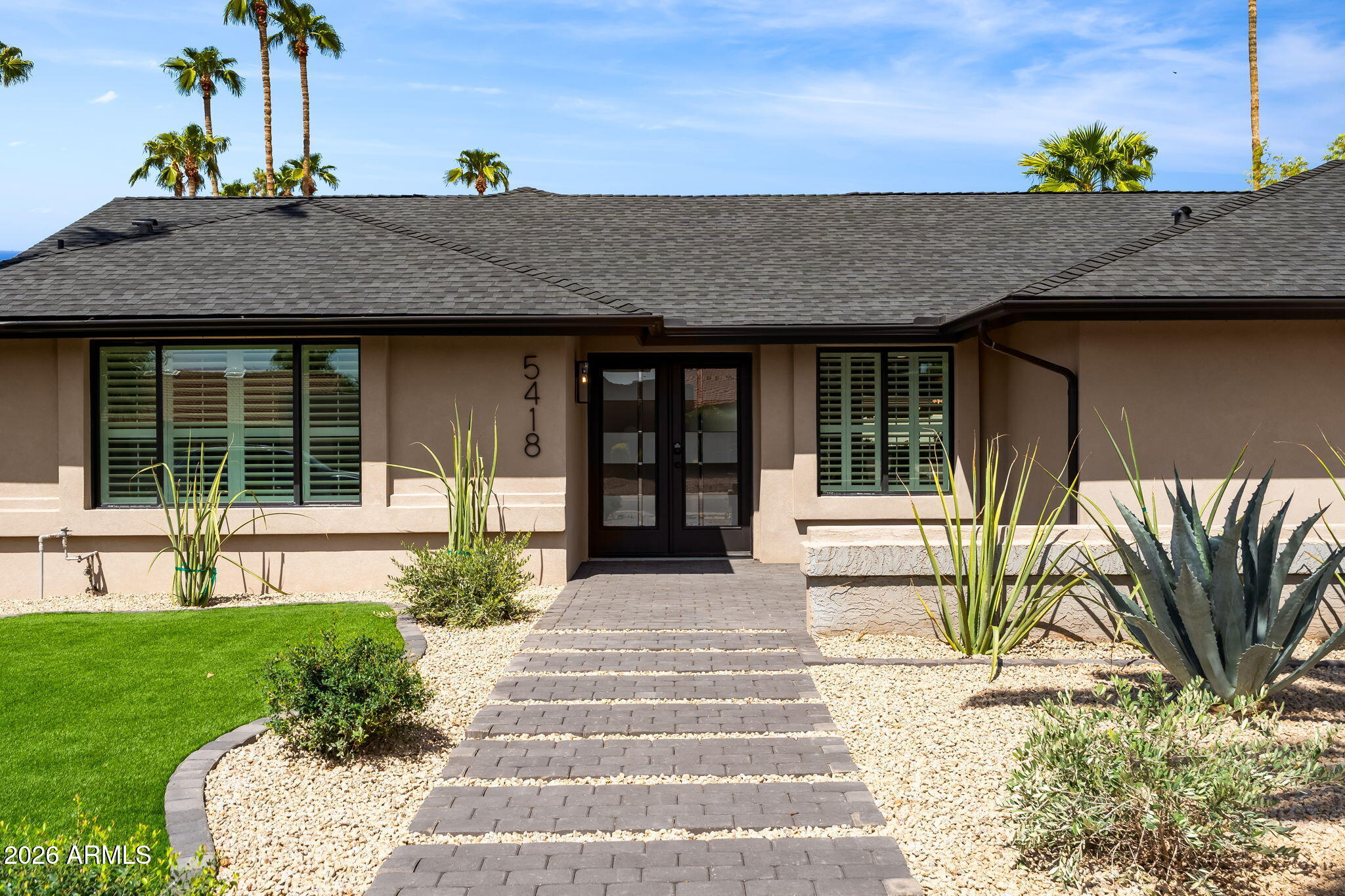 Single-story home with a black-framed entry, paved walkway, and desert landscaping.