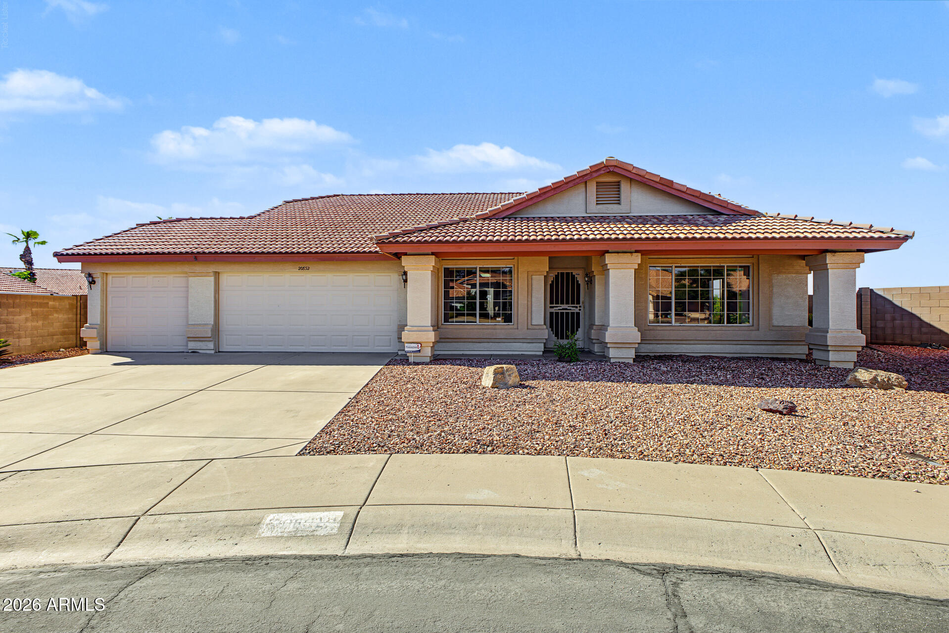 Single-story beige home with a red tile roof, three-car garage, and gravel landscaping.