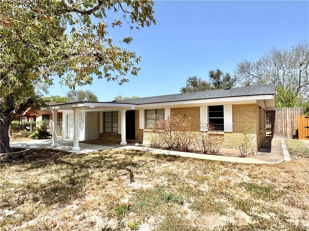 Single-story brick home with a covered carport, broad front lawn, and mature shade tree.