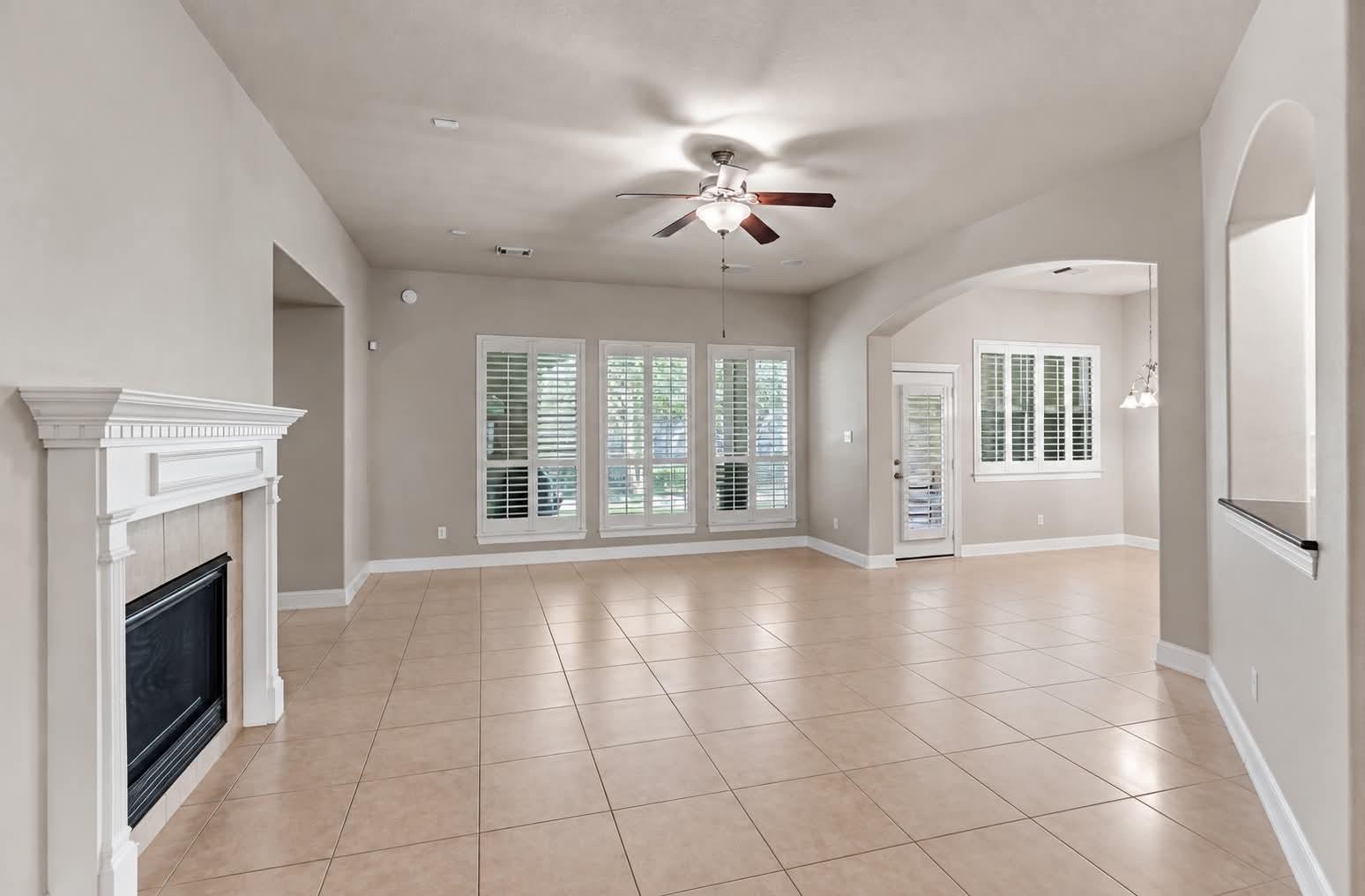 Empty living room with tiled floors, a white fireplace, shuttered windows, and an arched opening.