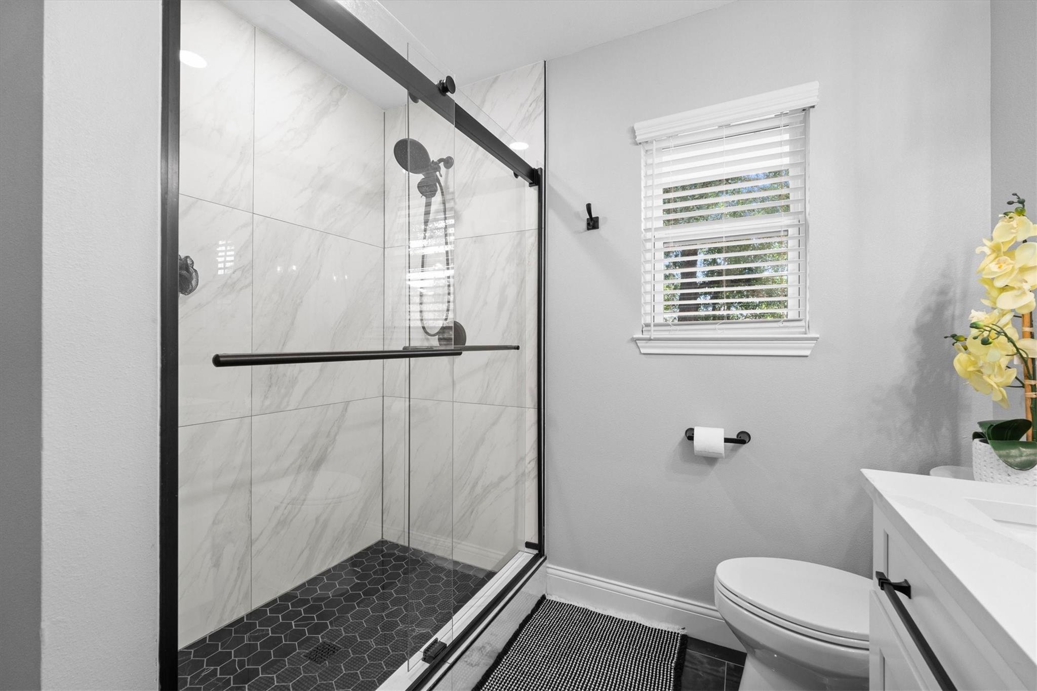 Bathroom with a glass walk-in shower, marble-look tile, and dark hexagonal floor.