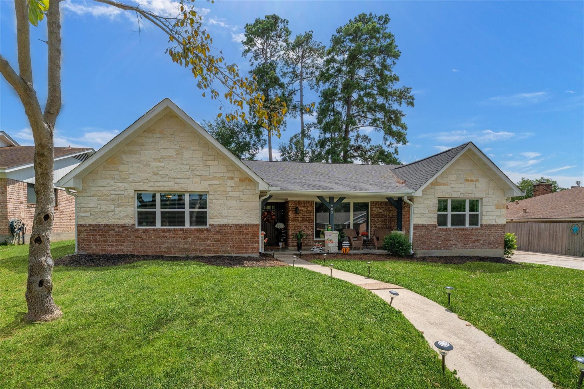 Single-story stone-and-brick house with a covered porch and curved walkway across a green lawn.