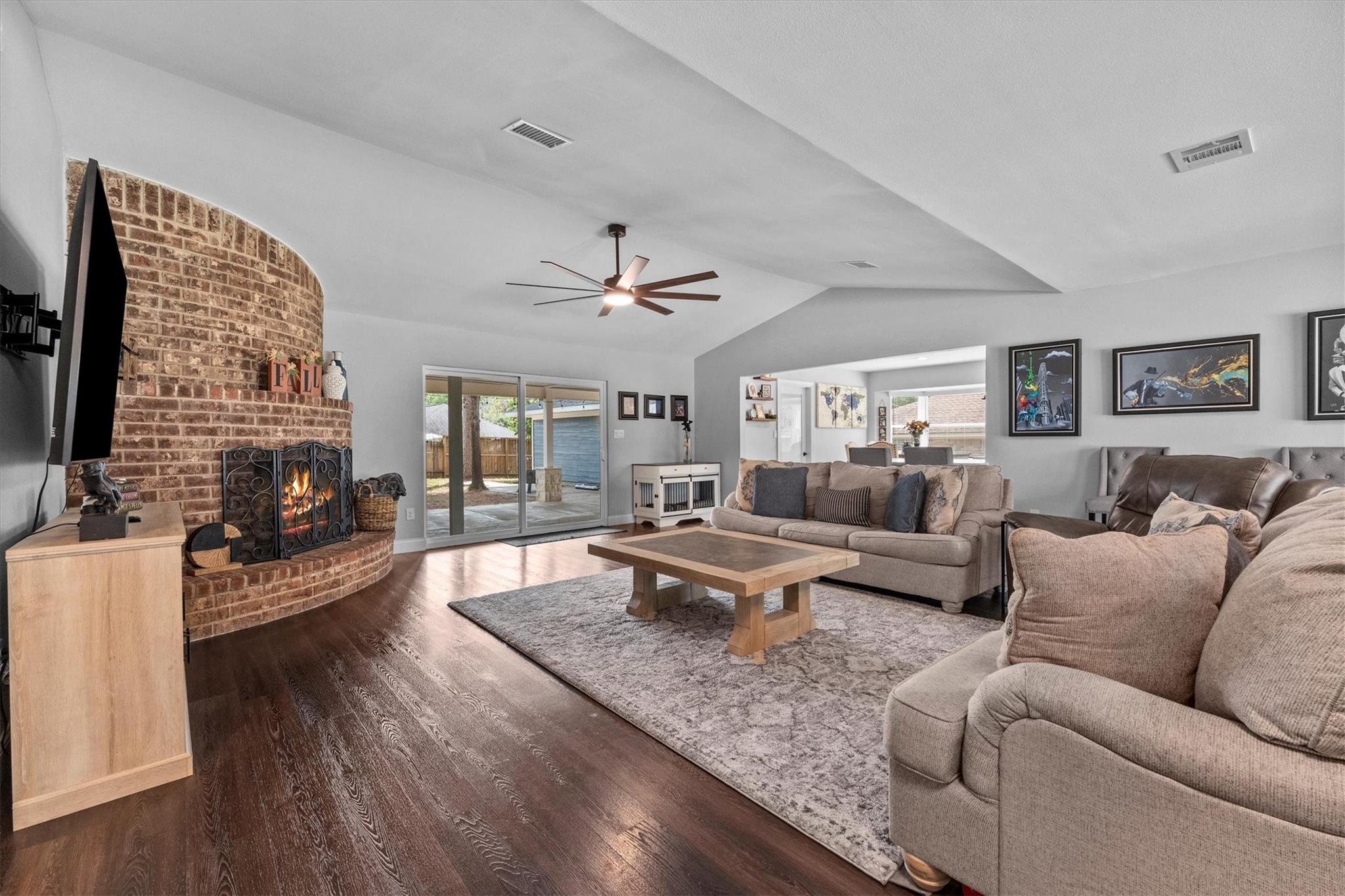 Living room with a curved brick fireplace, dark wood floors, and sliding glass doors to the backyard.