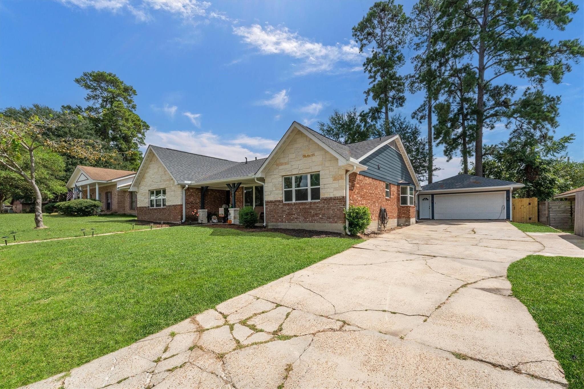 Single-story stone and brick home with a covered porch, attached garage, and cracked concrete driveway.