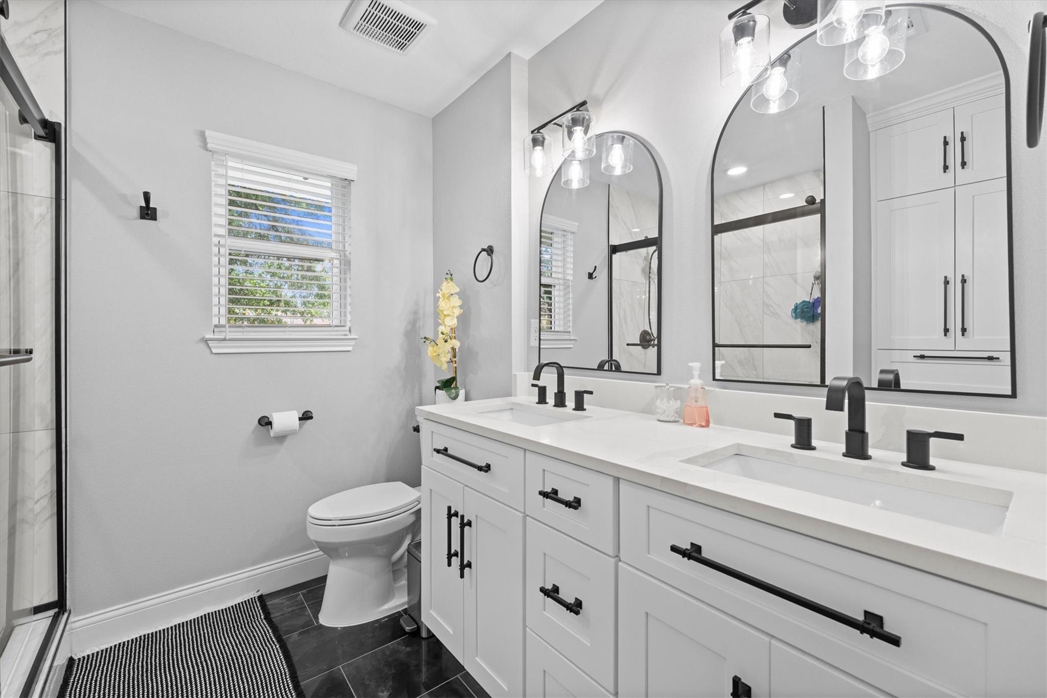 Bathroom with a white double-sink vanity, black fixtures, arched mirrors, and a glass shower.