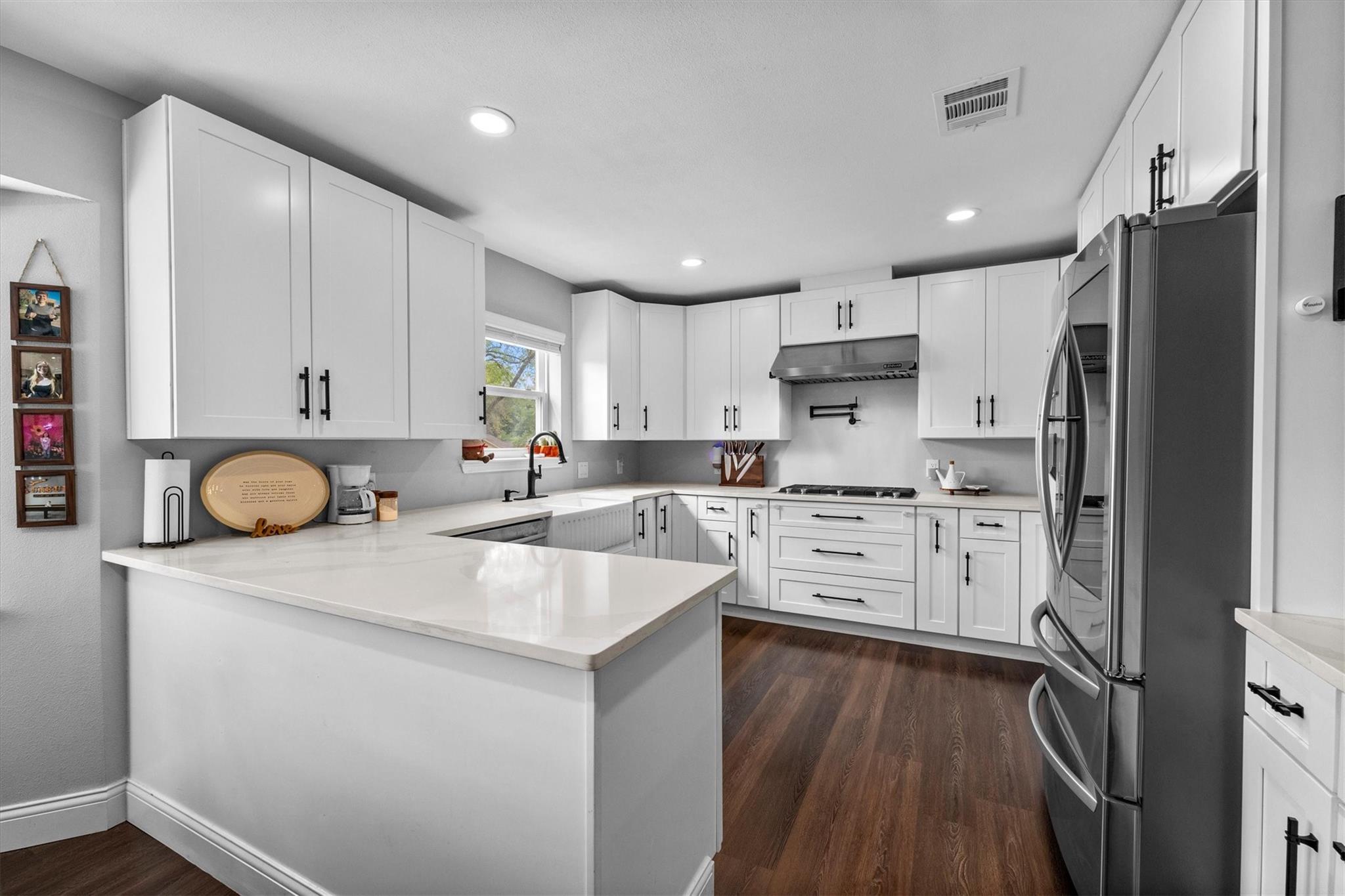 Bright kitchen with white cabinets, a large island, stainless steel appliances, and dark wood floors.