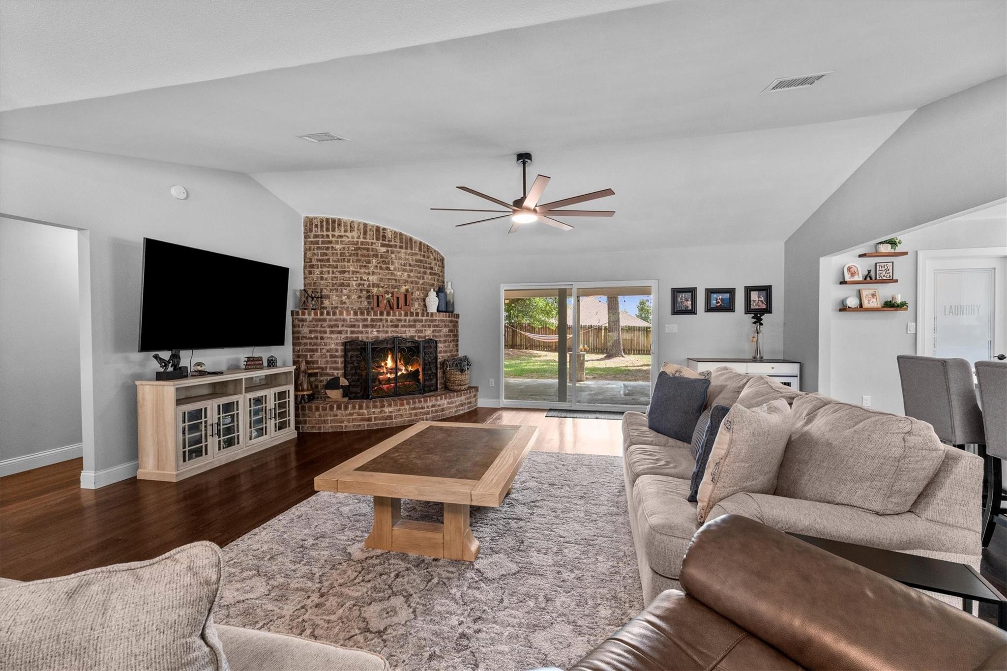 Furnished living room with a curved brick fireplace, large rug, and sliding doors to the backyard.