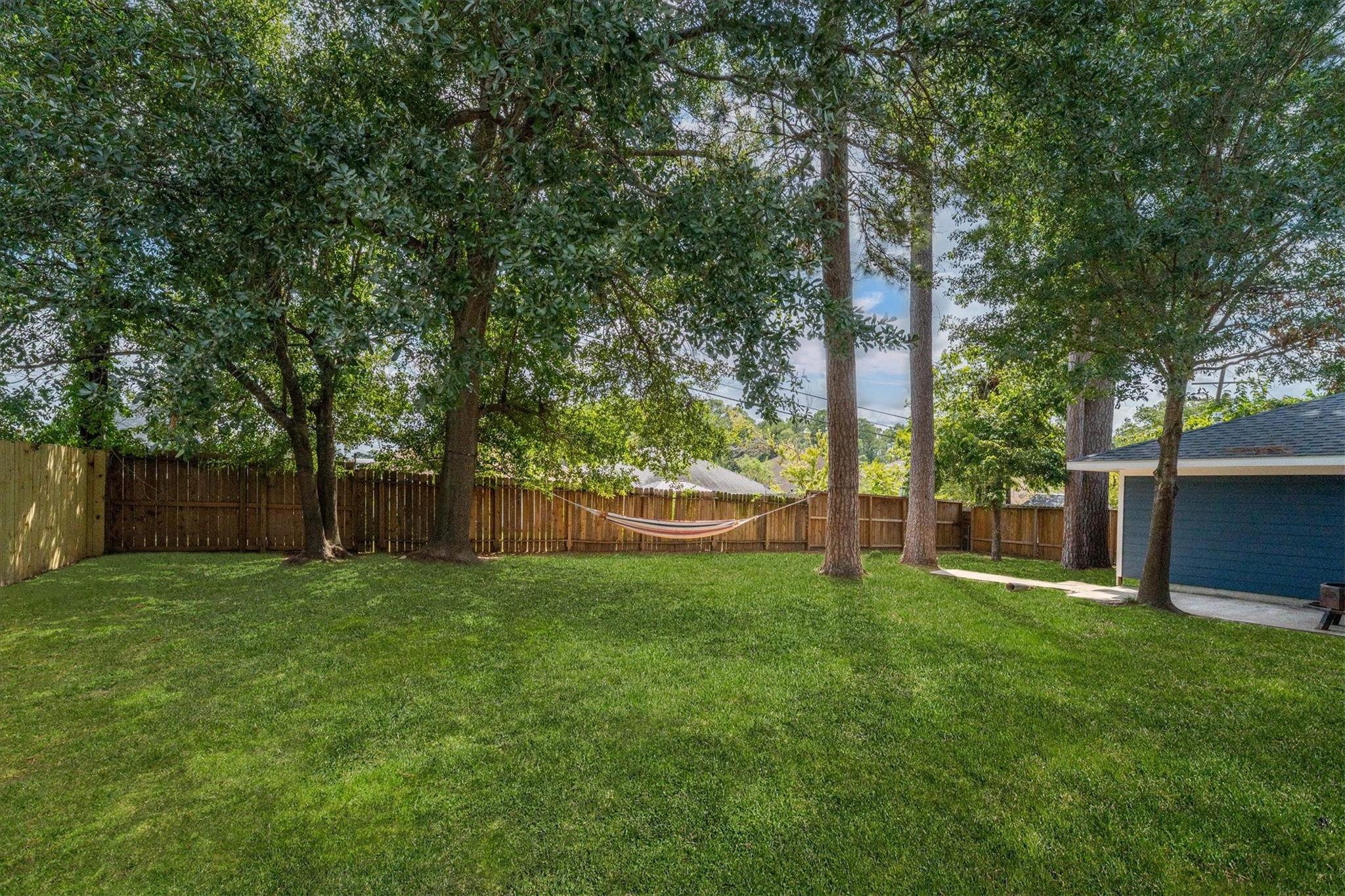 Fenced grassy backyard with mature trees and a hammock beneath the shade.