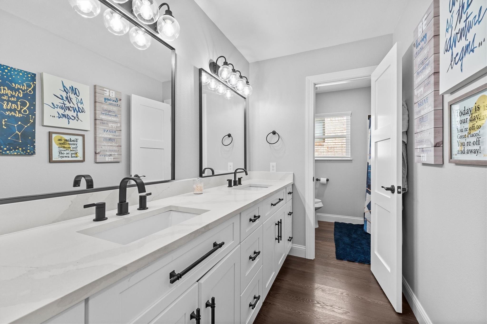 Bathroom with a long double vanity, white cabinetry, black fixtures, and large illuminated mirrors.