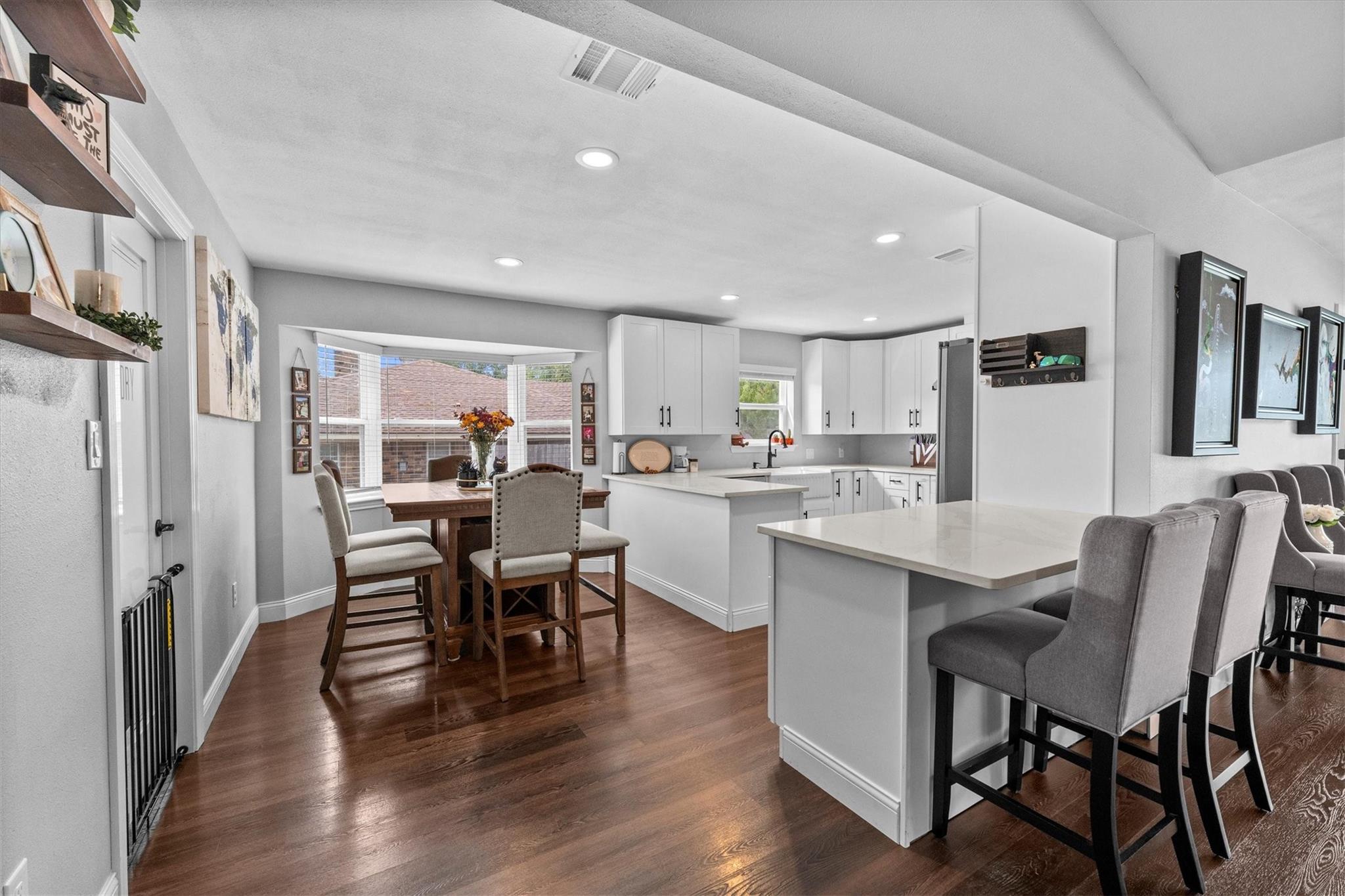 Kitchen and dining area with white cabinetry, a large island, and dark hardwood floors.